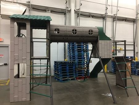 A playground set in a warehouse with blue pallets in the background