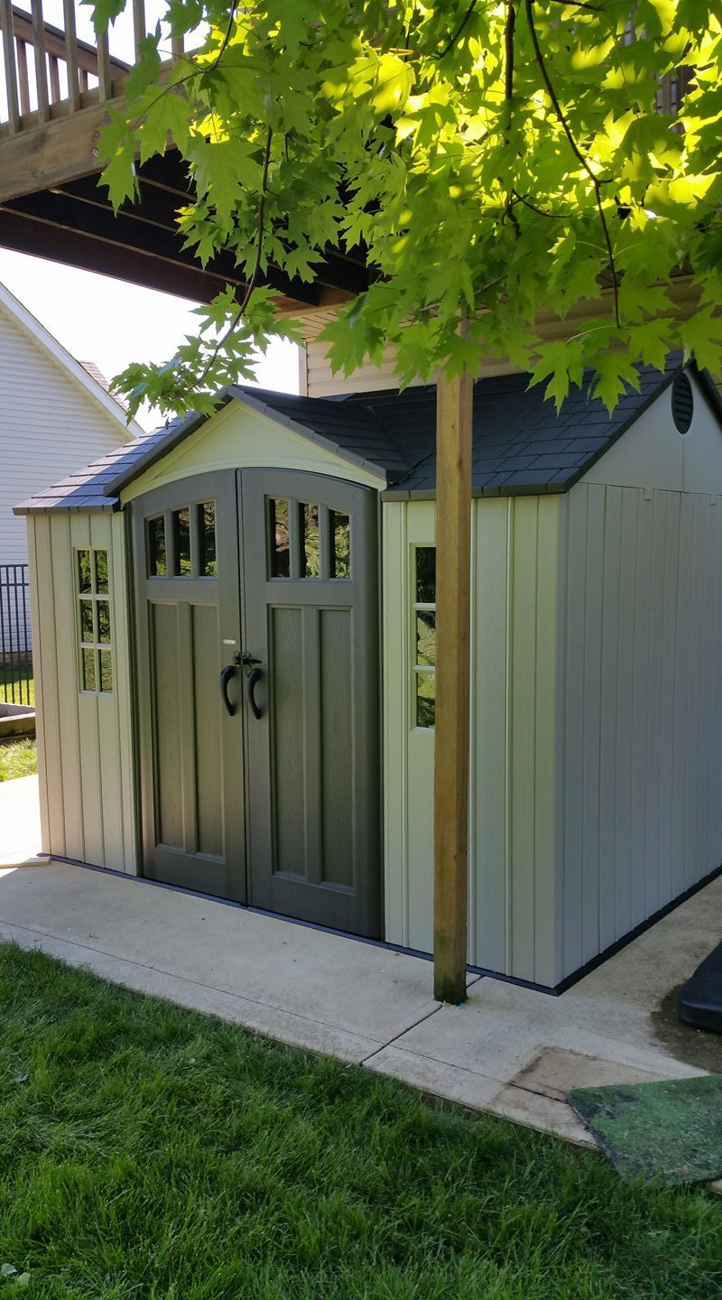 A white and gray shed is sitting in the grass next to a house.