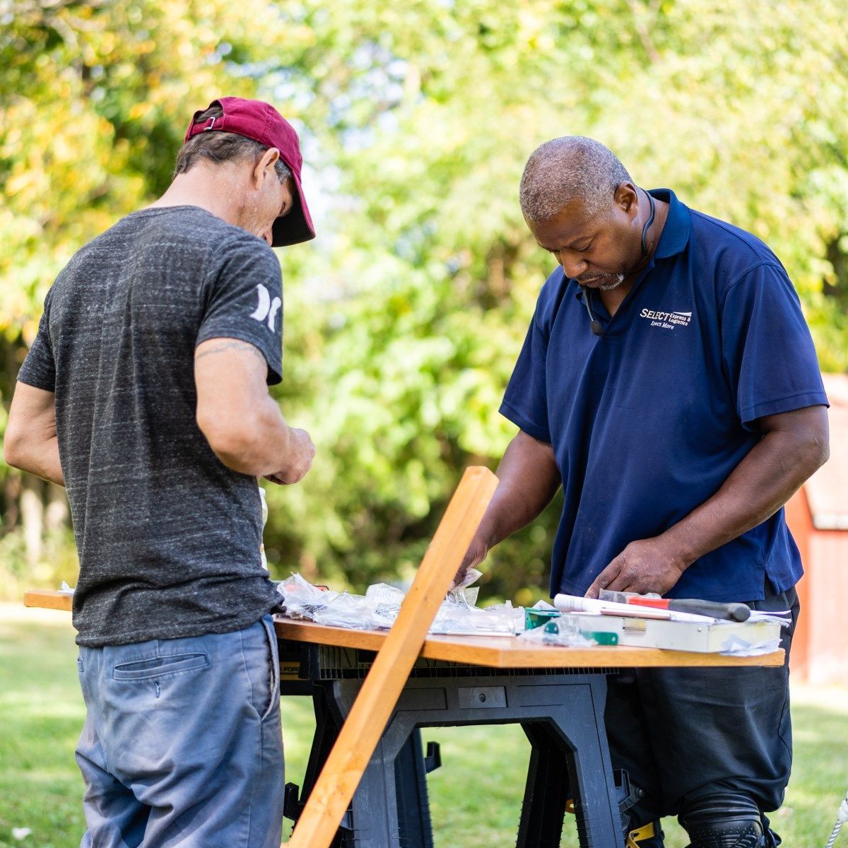 Two men are working on a wooden table outside