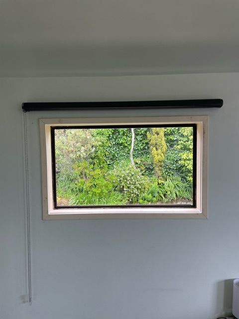 A Large Window with a Black Blind on it in a Room with Trees in the Background — Lower Hutt, NZ — Complete Aluminium Maintenance Ltd