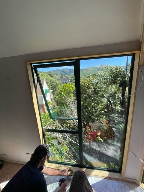 A Man is Sitting in Front of a Large Window with a View of Trees — Lower Hutt, NZ — Complete Aluminium Maintenance Ltd