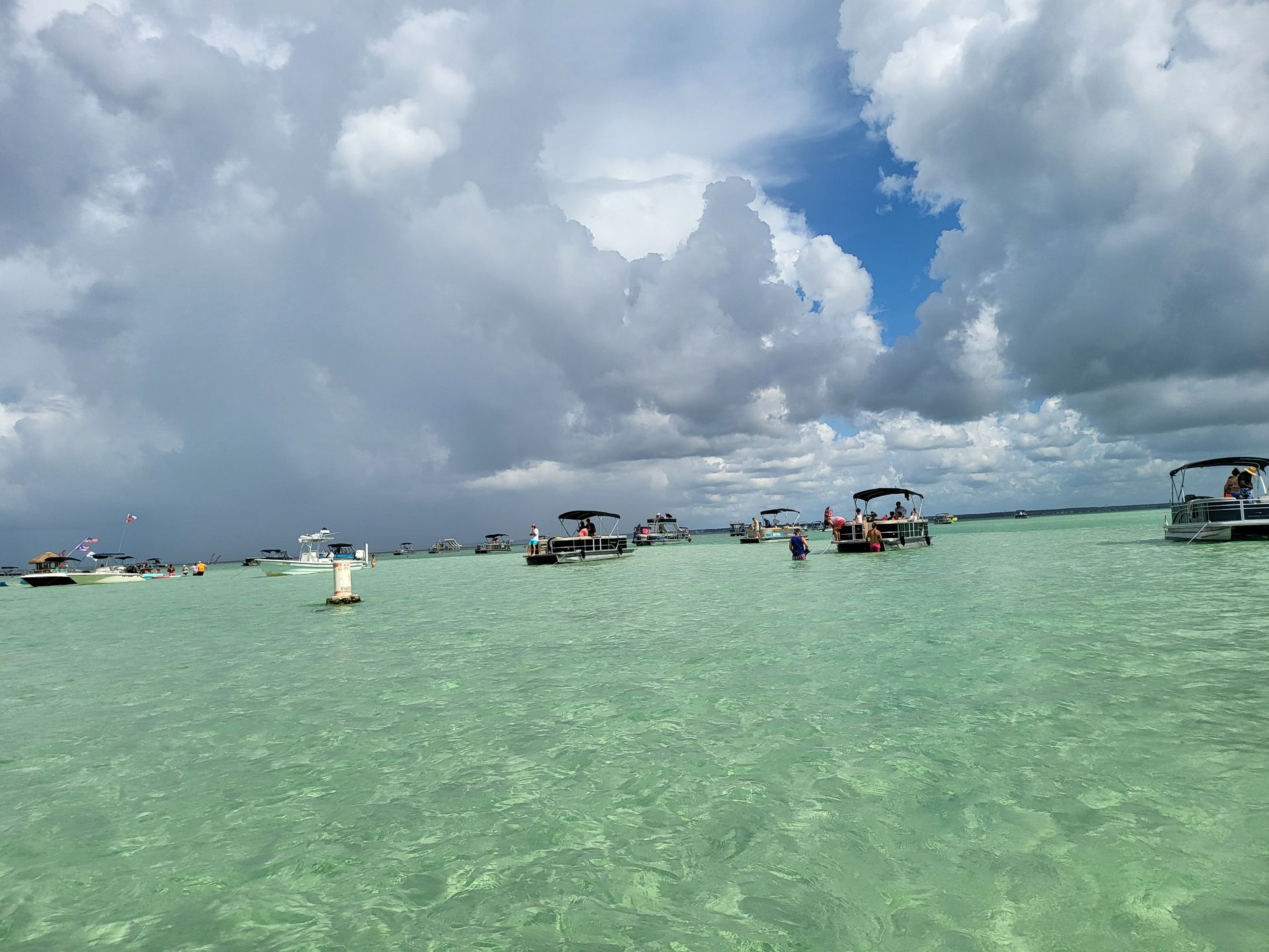 Boats and people in shallow, turquoise water under a cloudy sky.