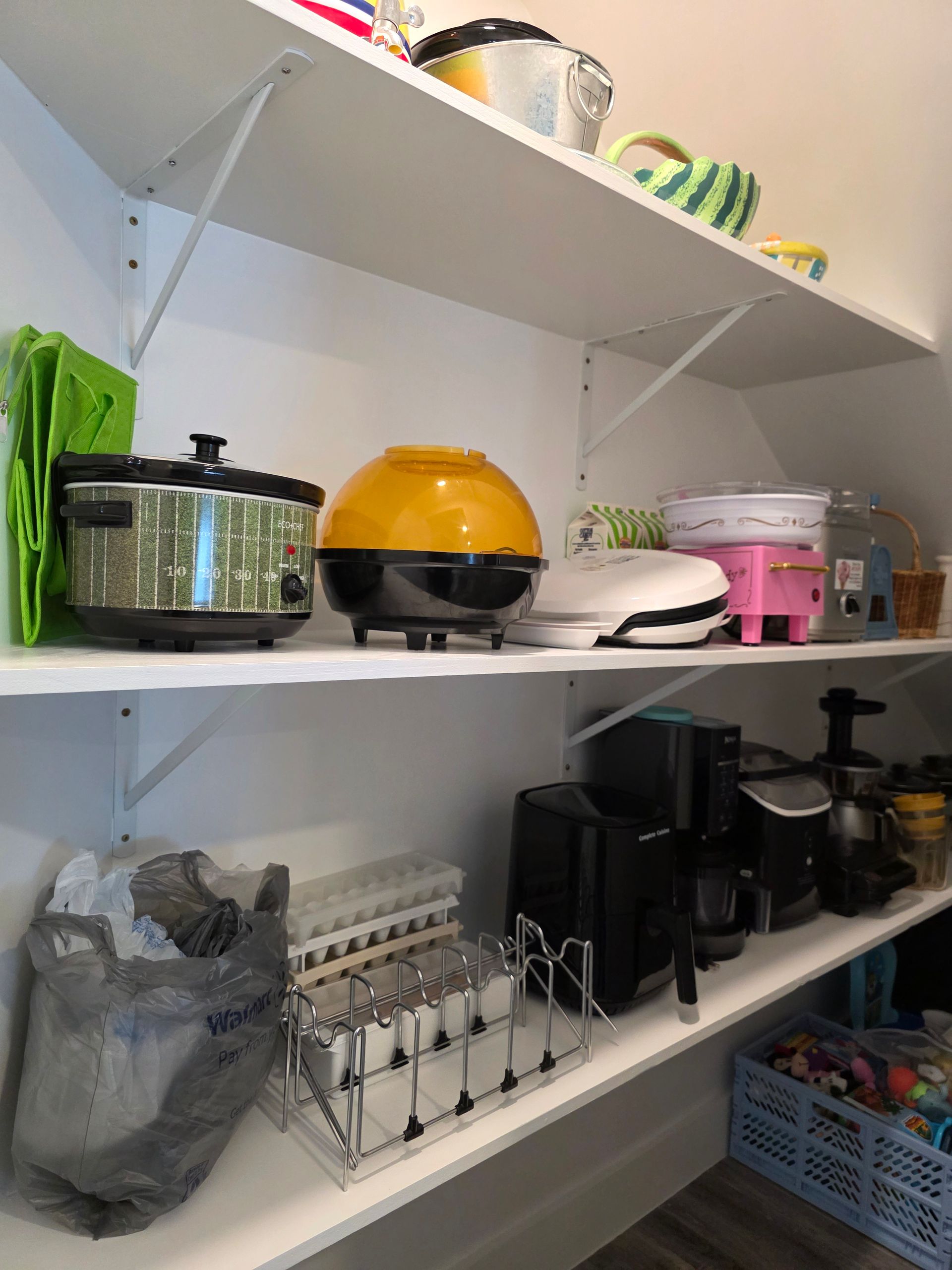 White pantry shelves filled with small kitchen appliances, including a slow cooker and popcorn maker.