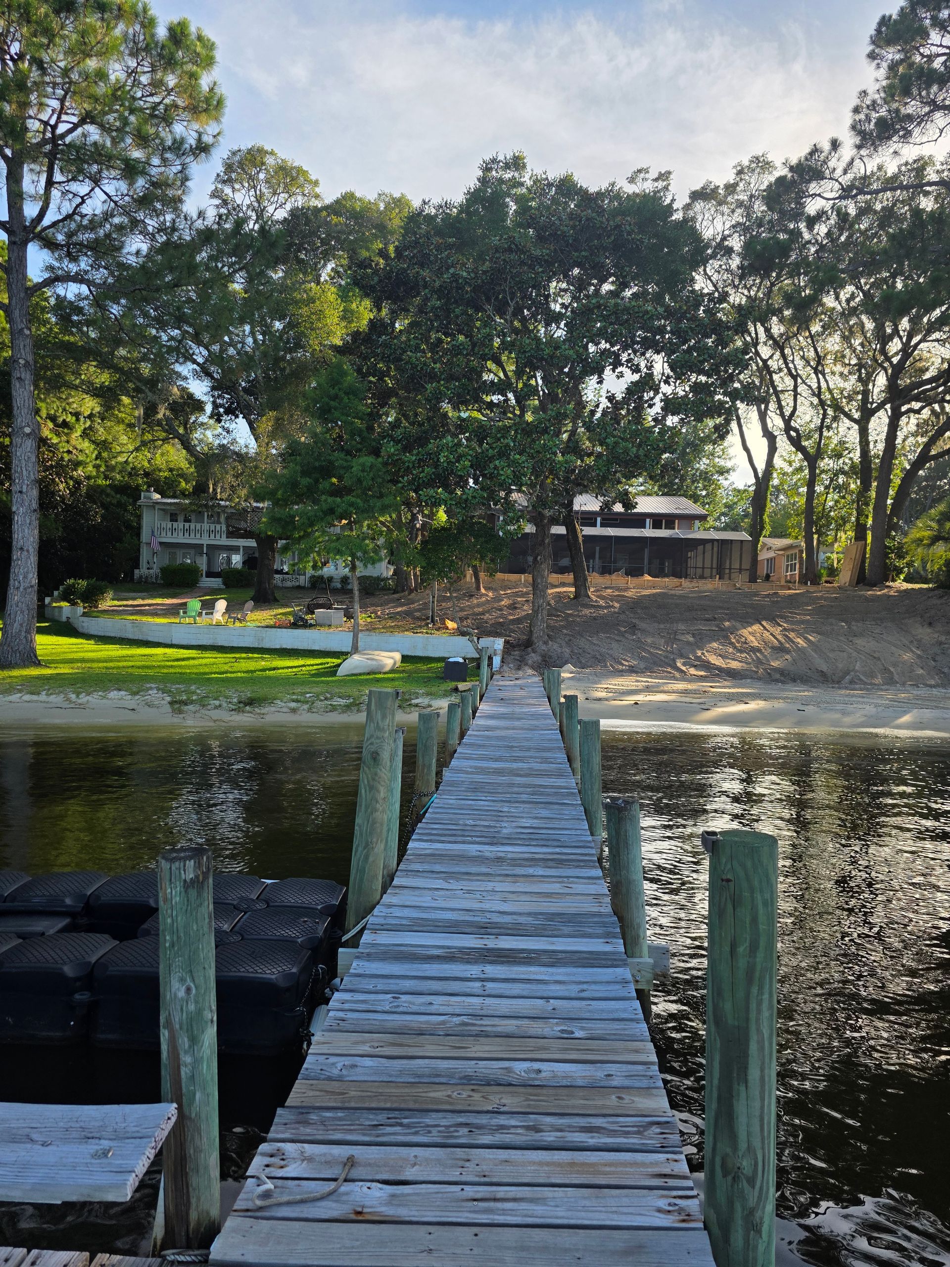 Wooden dock leading to shore with trees and a house on the edge of the water.