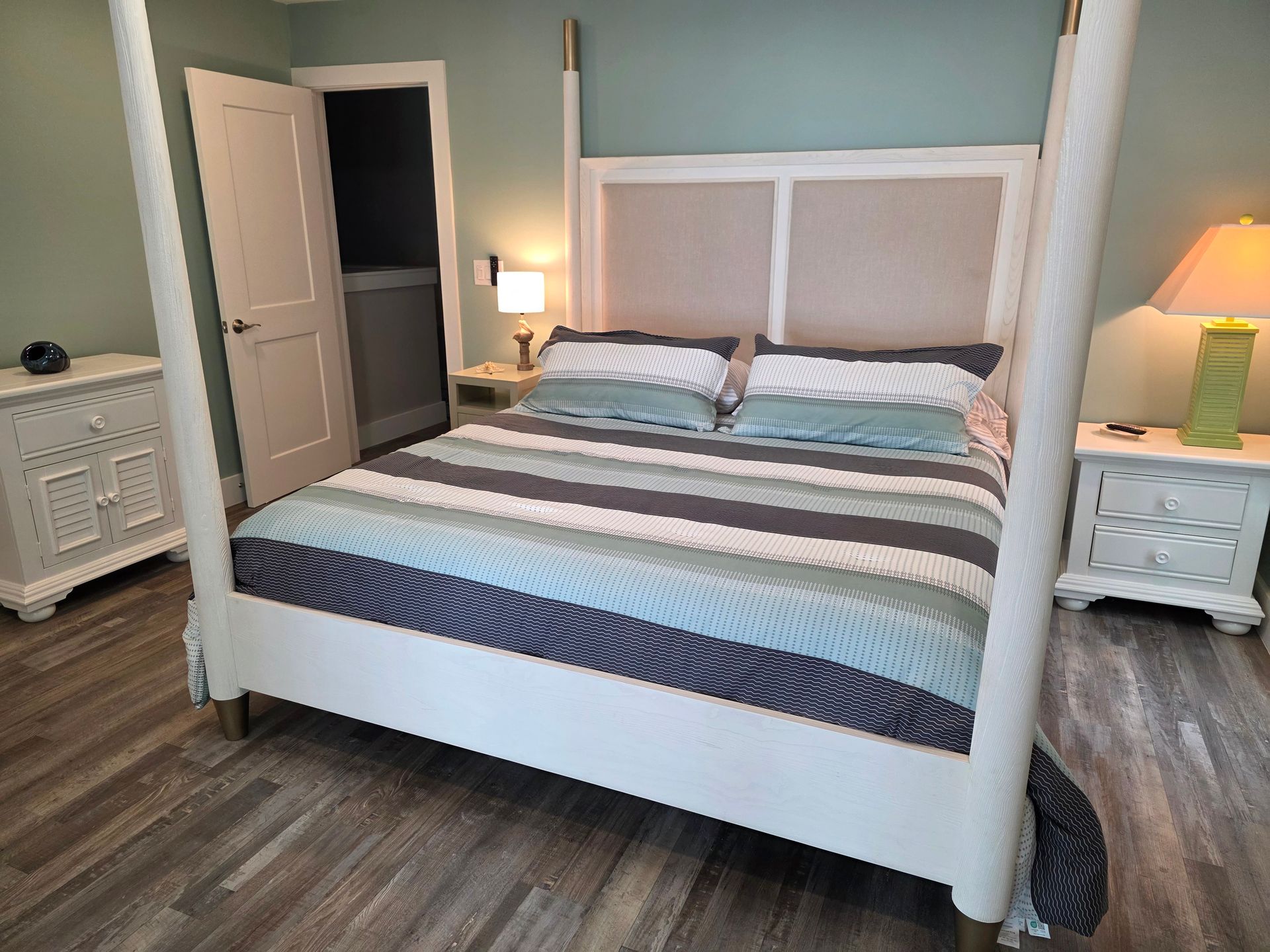 Bedroom with a white four-poster bed, blue, gray and white striped bedding, and two white nightstands.