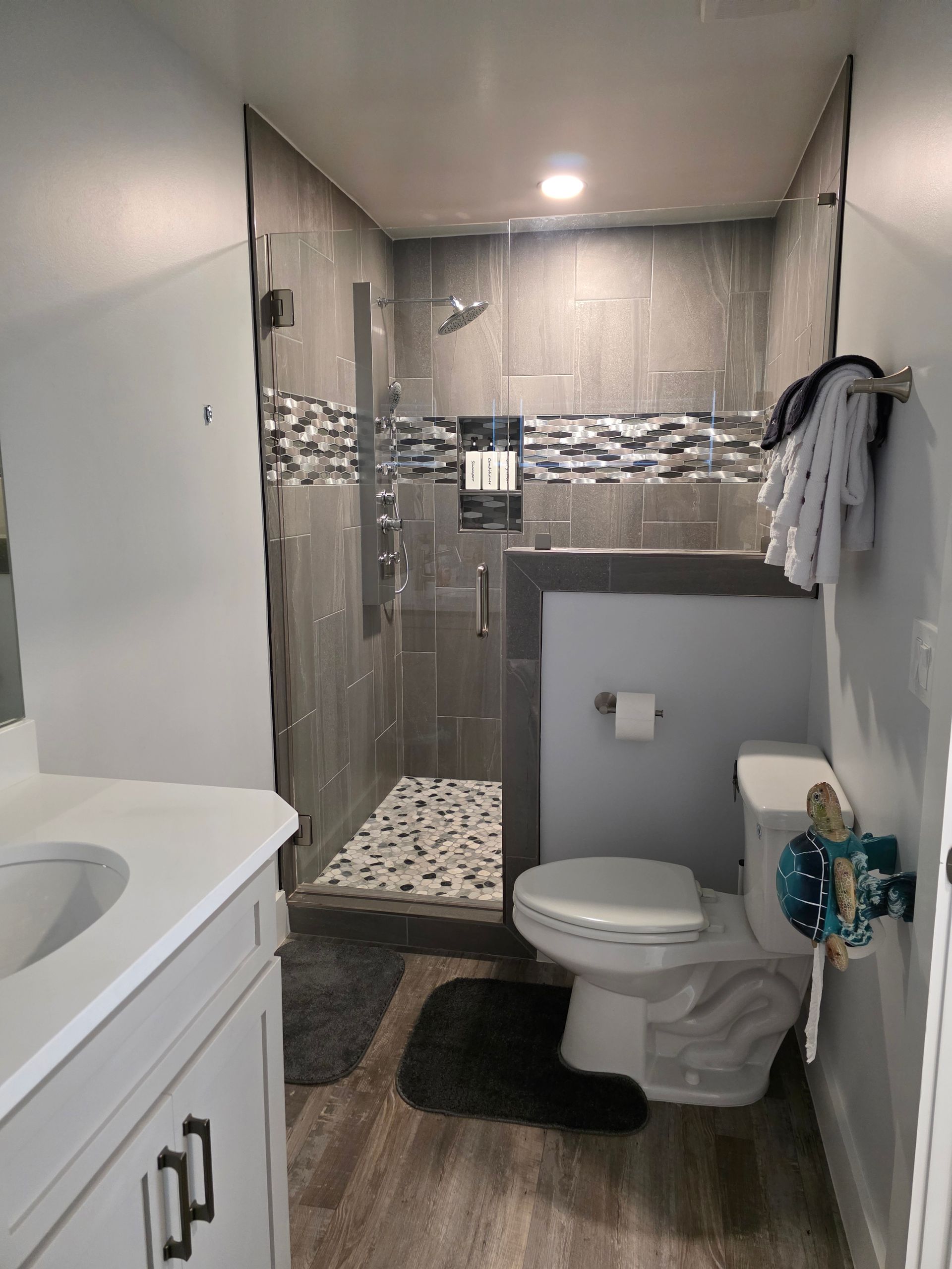 Modern bathroom with a gray tile shower, toilet, and white vanity.