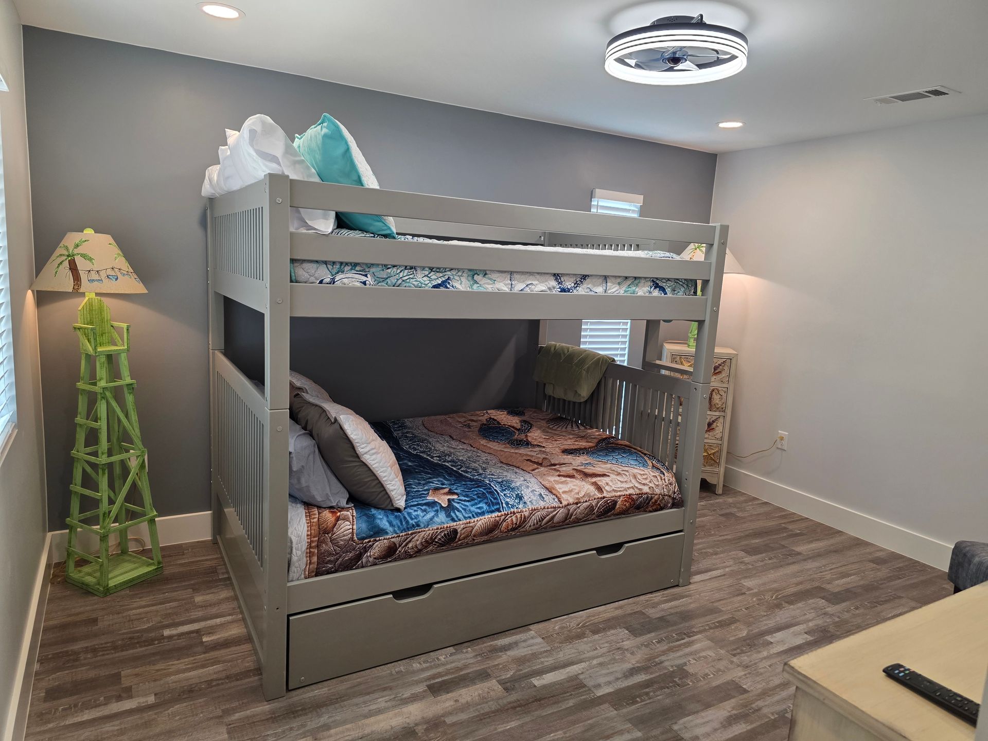 Gray bunk beds in a bedroom with a green lamp and fan.