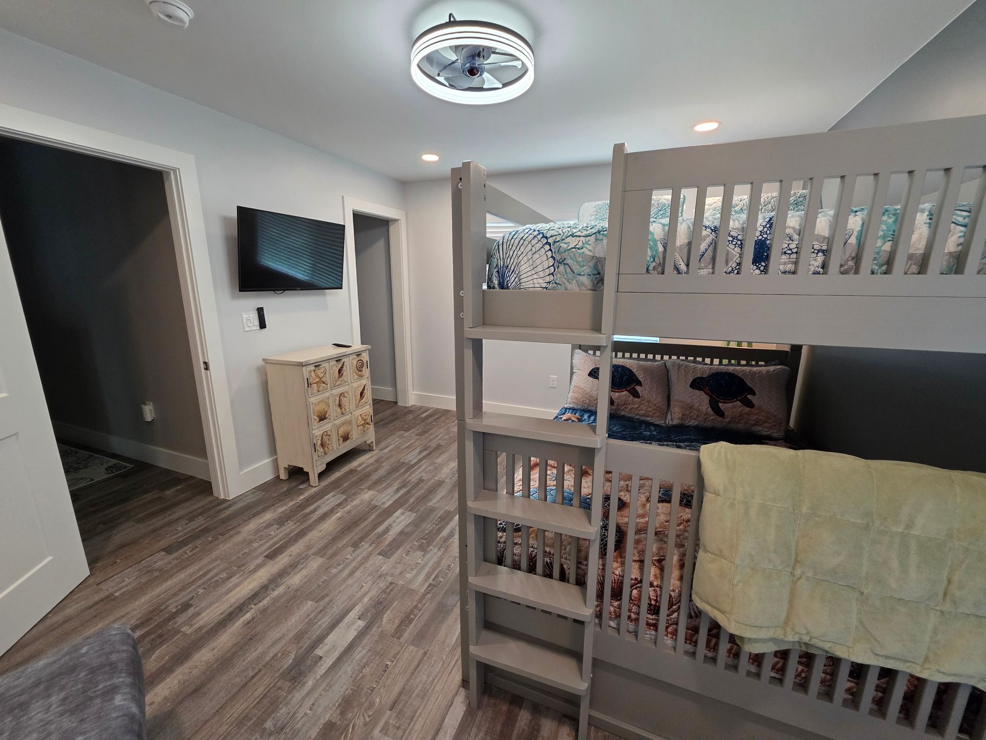 Bunk beds in a light grey room with a dresser and a wall-mounted TV.