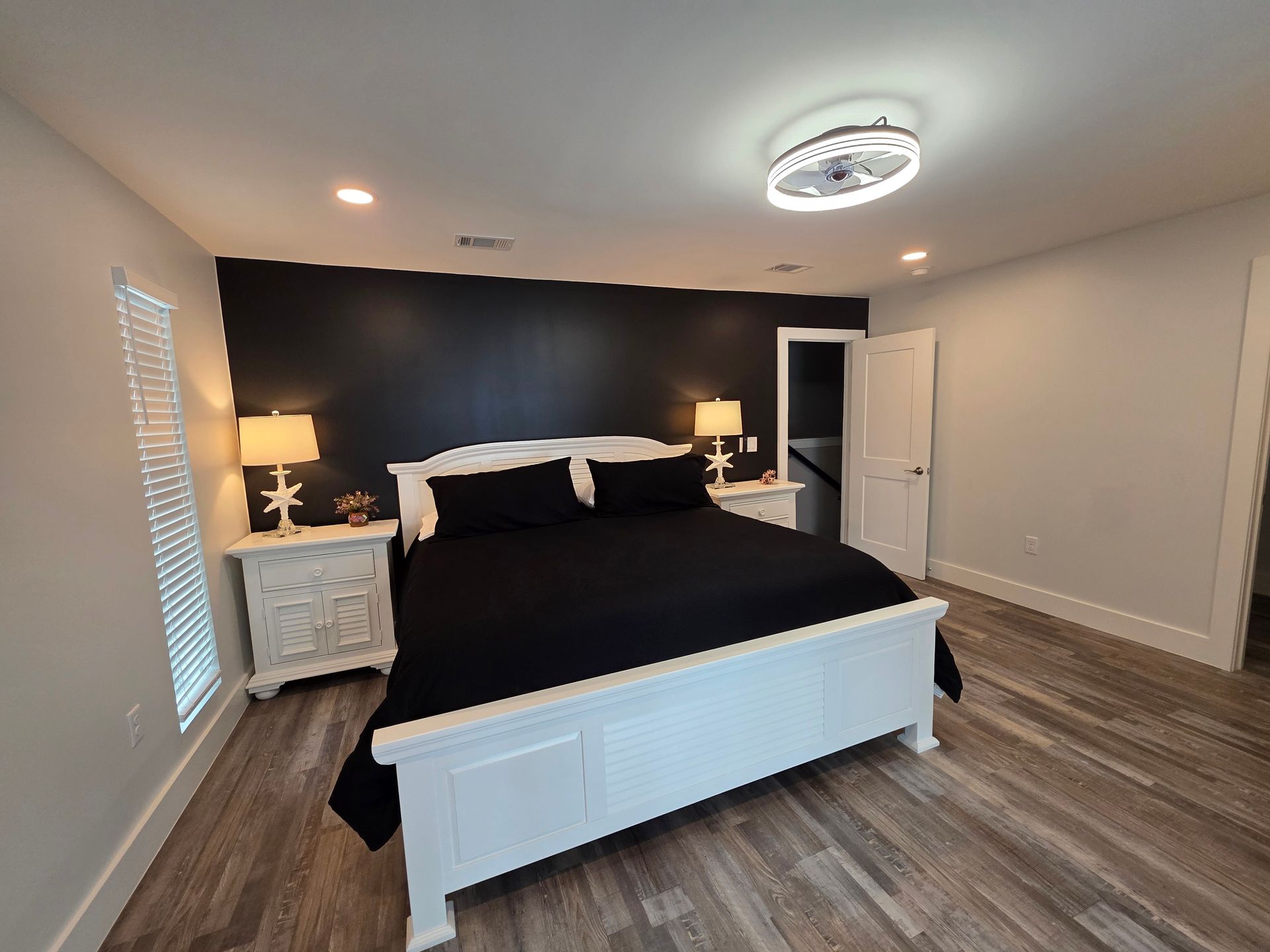 Bedroom with white bed, black bedding, nightstands, dark accent wall, and wood-look flooring.