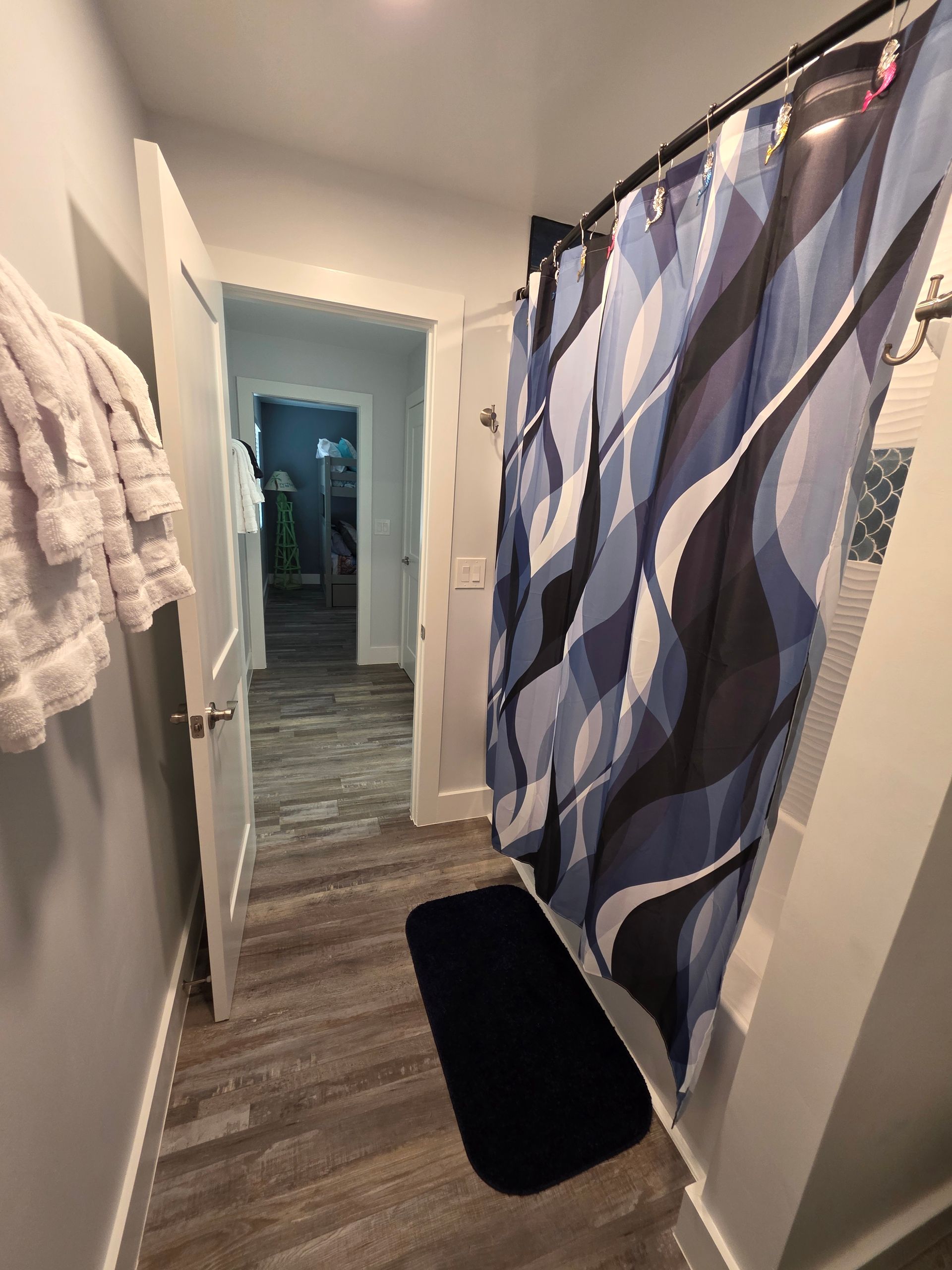 Bathroom with blue shower curtain, gray walls, and wooden floor. Towels hang on the left.