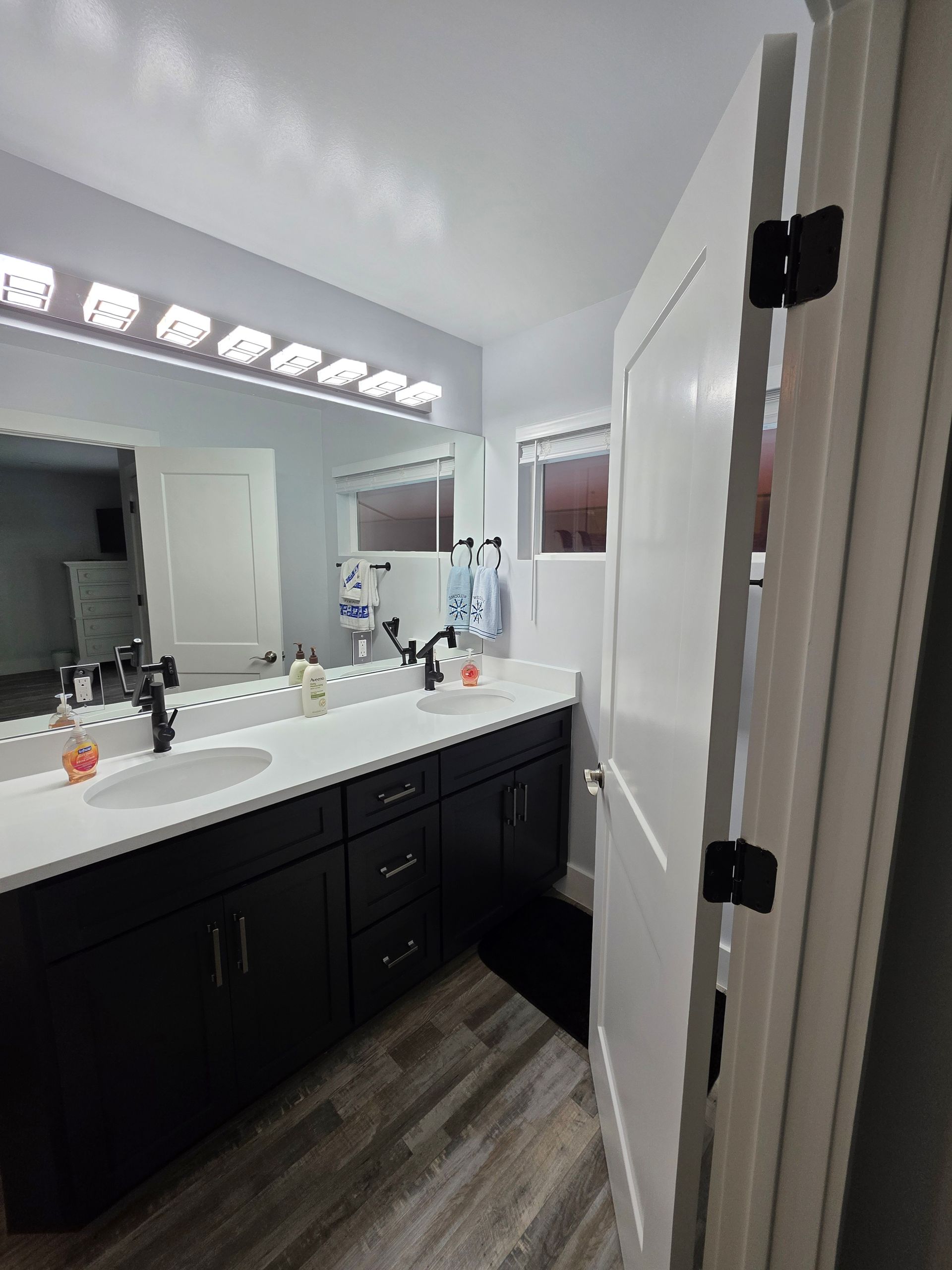 Bathroom with a black vanity, white countertop, large mirror, and a partially open white door with black hinges.