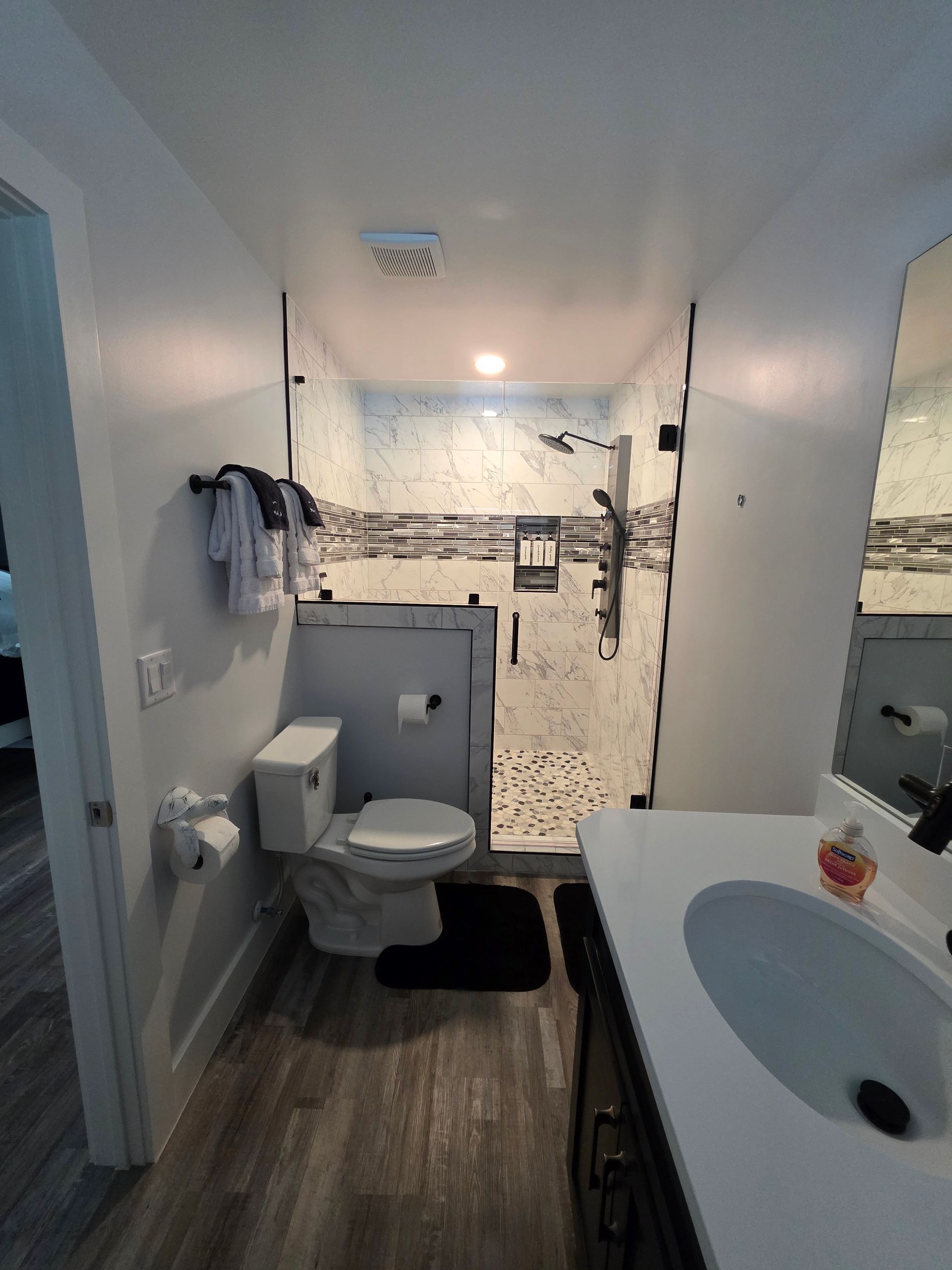 Bathroom with white walls, dark floor. Toilet, shower with glass door, and sink with mirror.