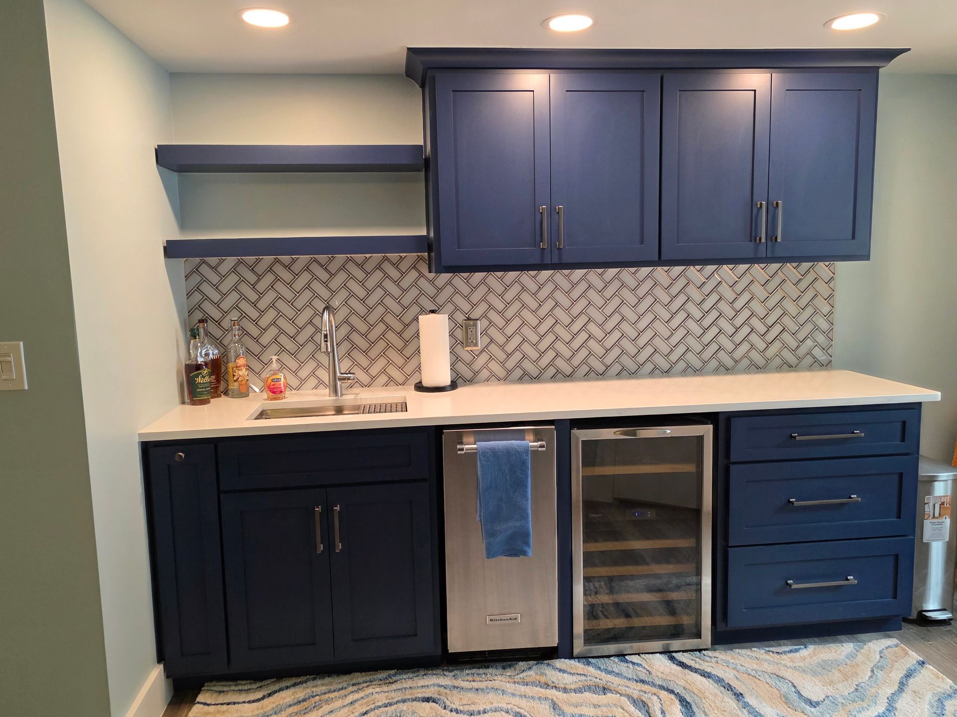 A modern navy blue wet bar with white countertop and a decorative tile backsplash.