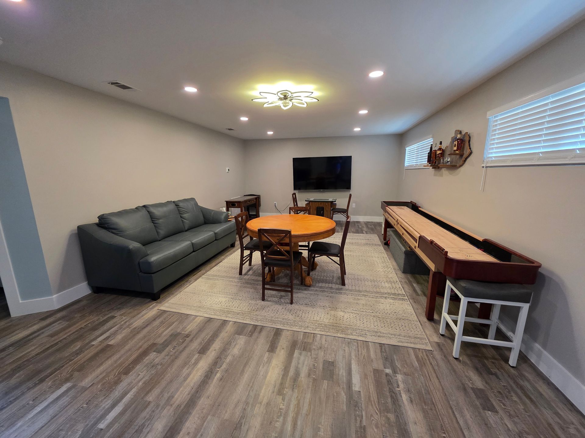 A finished basement with a blue couch, round table, shuffleboard, and TV.