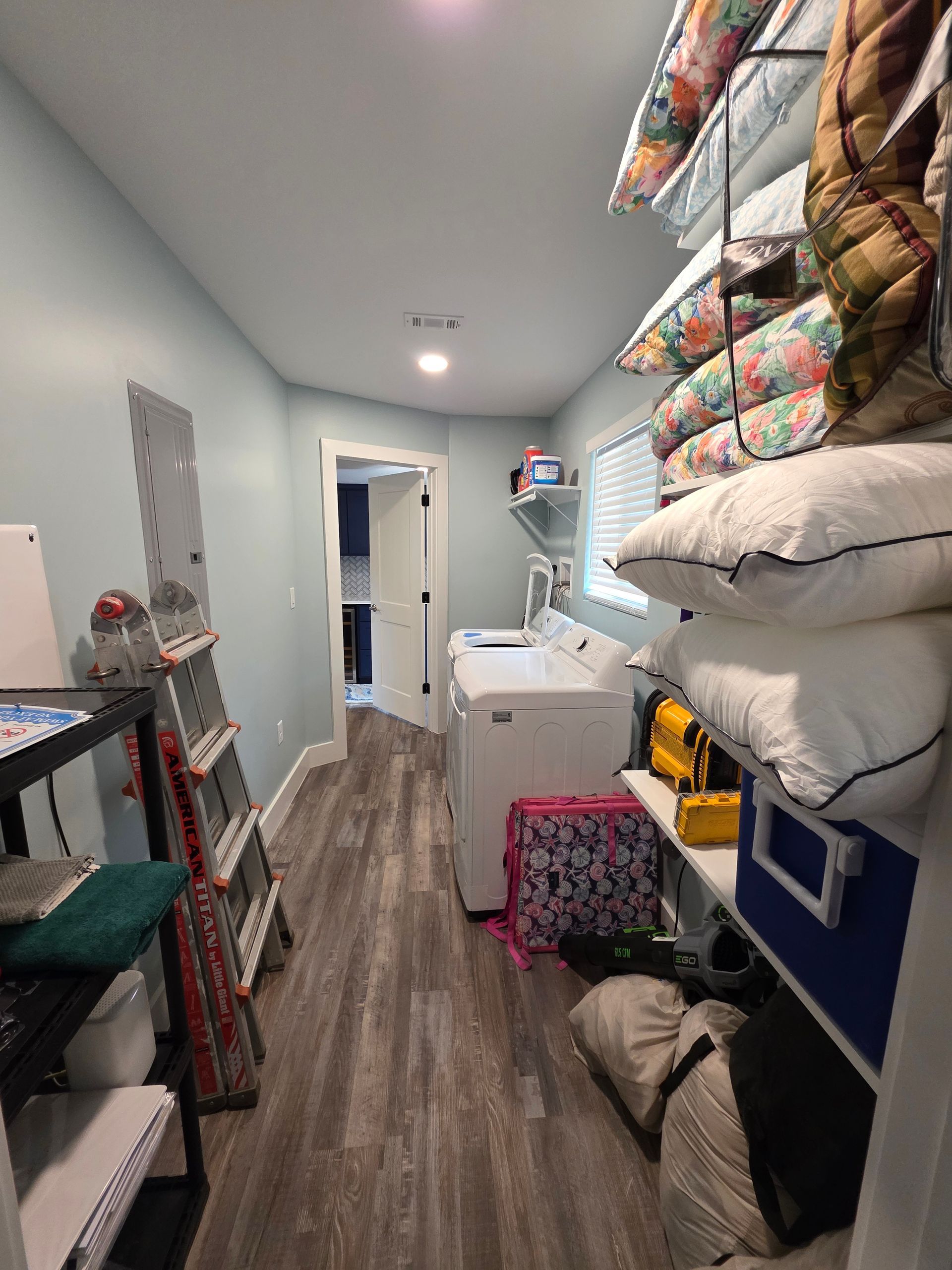 Narrow laundry room with a washer, pillows, shelves, and a door in the background.