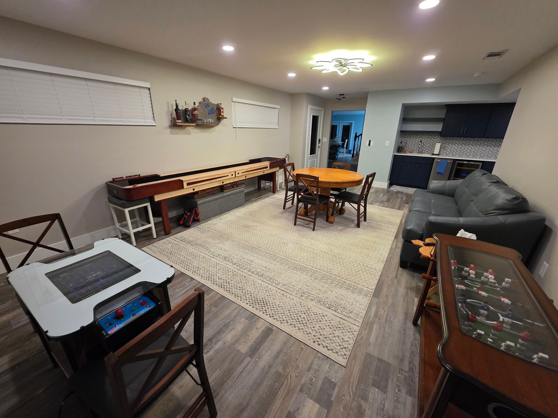 Game room with shuffleboard, table, couch, arcade games, and kitchen.