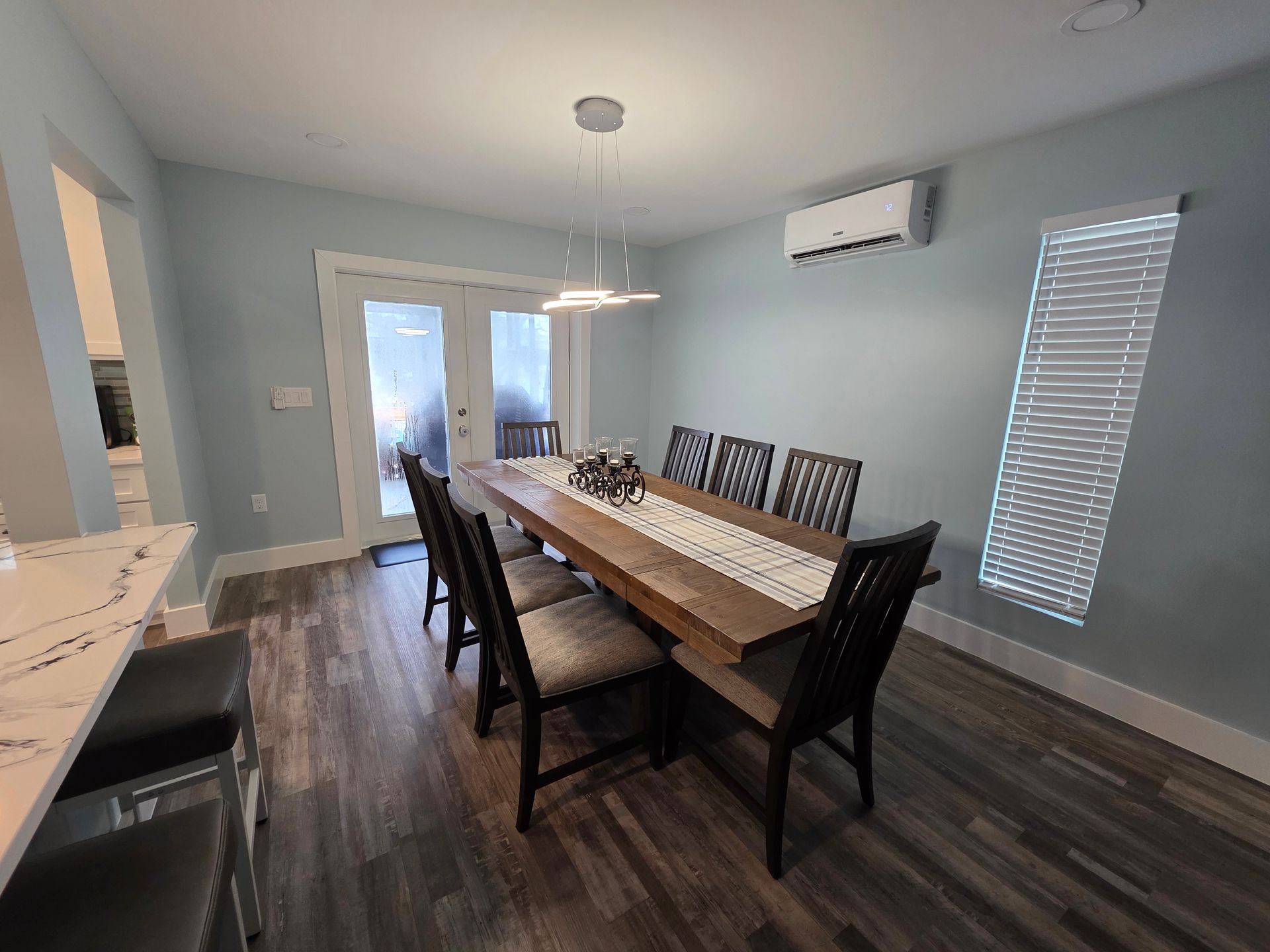 Dining room with a long wooden table, chairs, and sliding glass doors. Blue walls, a/c unit.