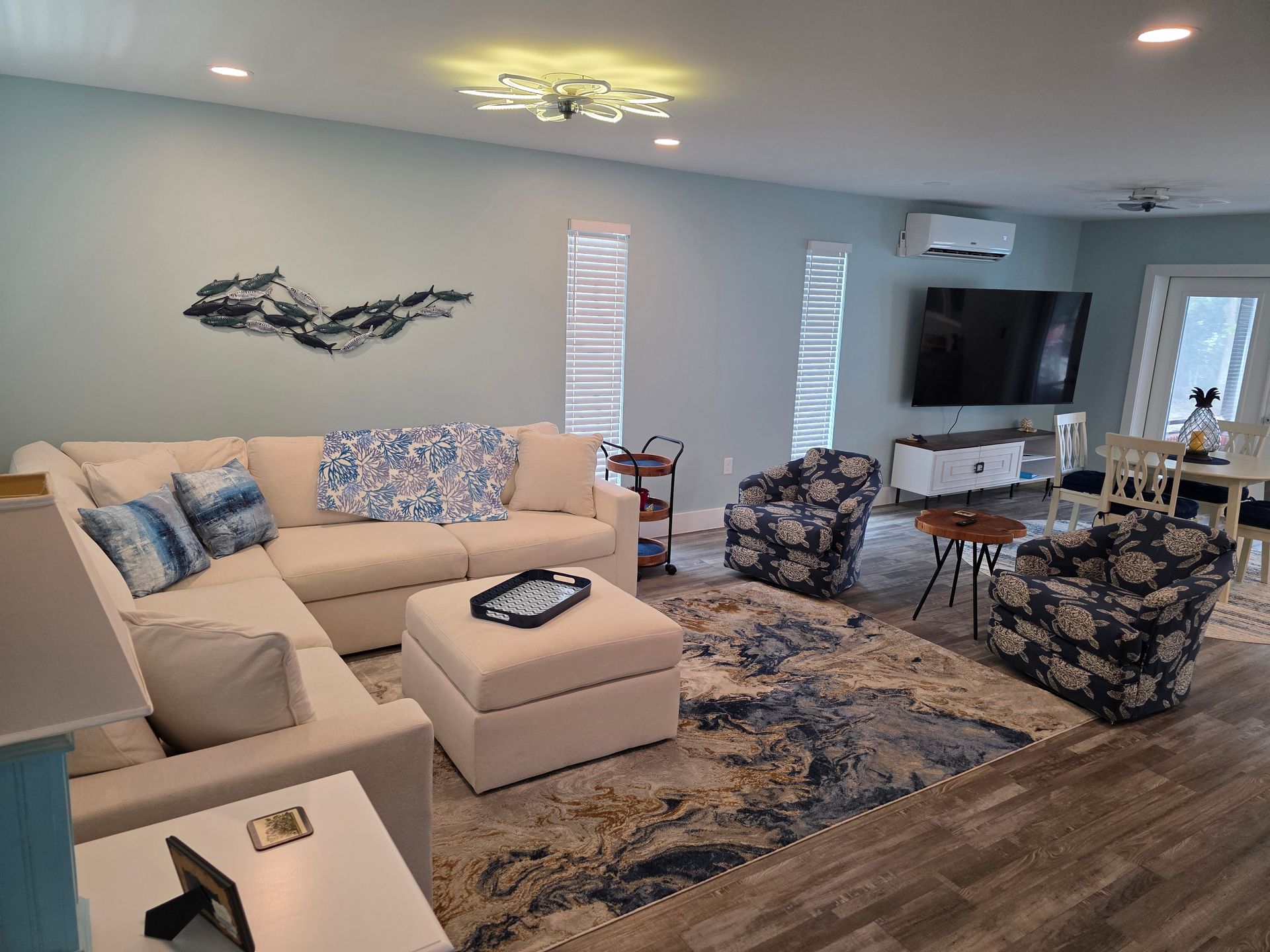 Living room with sectional sofa, patterned rug, two patterned chairs, TV, and decorative wall art.