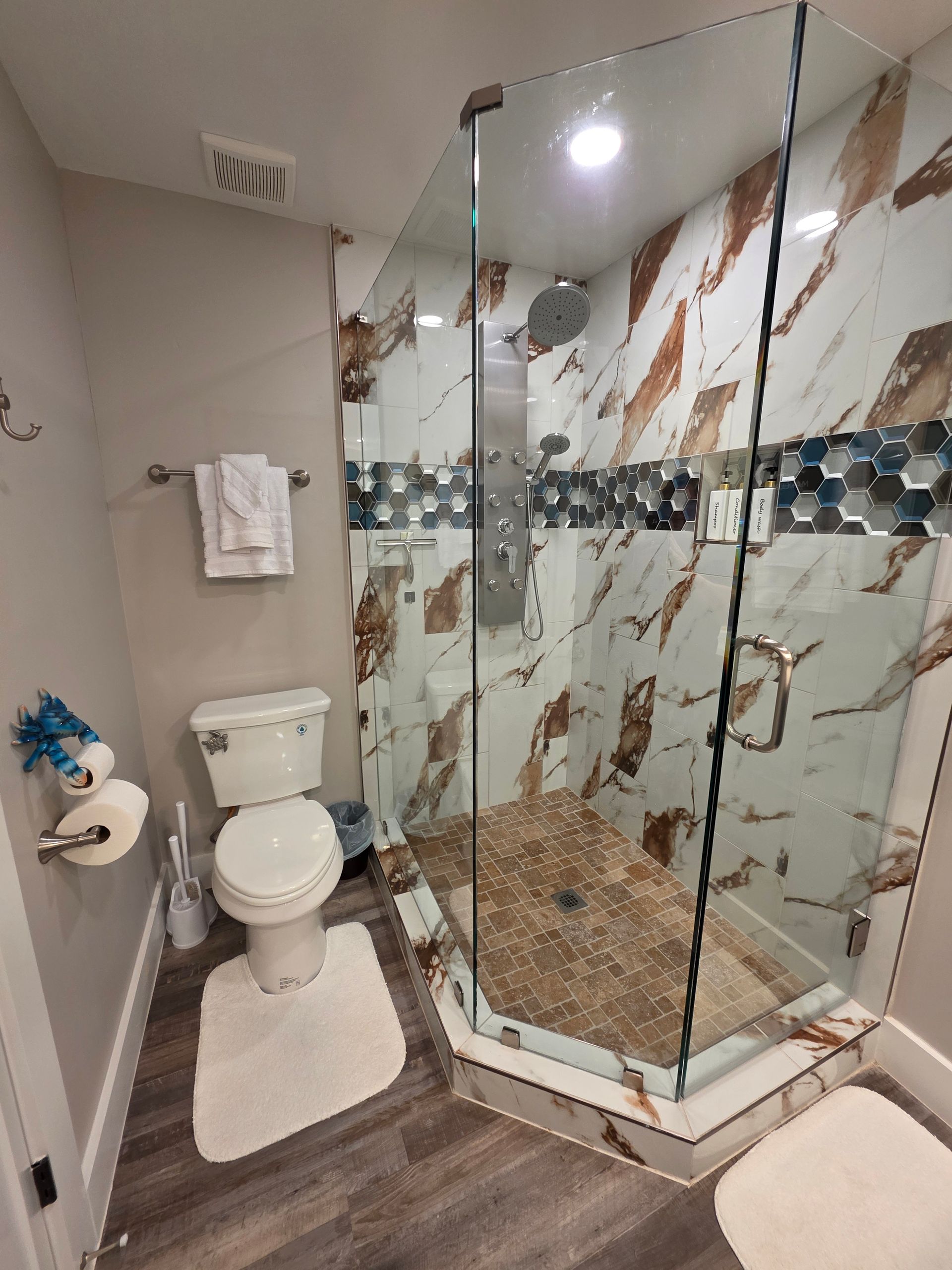 Small bathroom with a glass-enclosed shower, toilet, and gray and white marble tile.