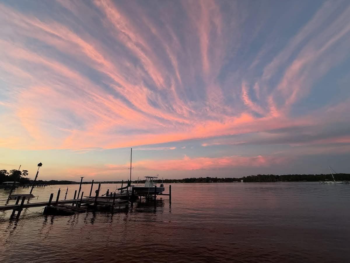Sunset over water with pink streaked clouds, docks, boats, and a radio tower.