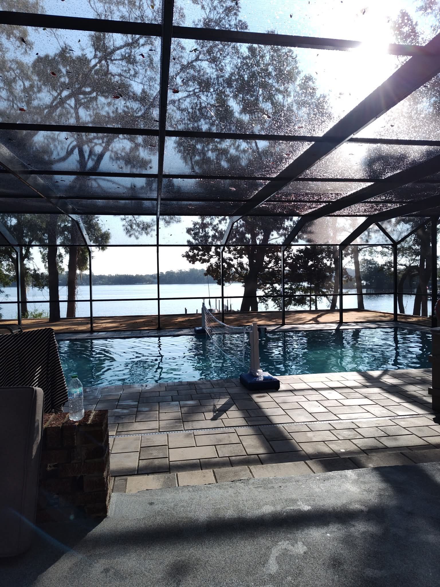 Pool under a screened enclosure, overlooking a lake and trees on a sunny day.
