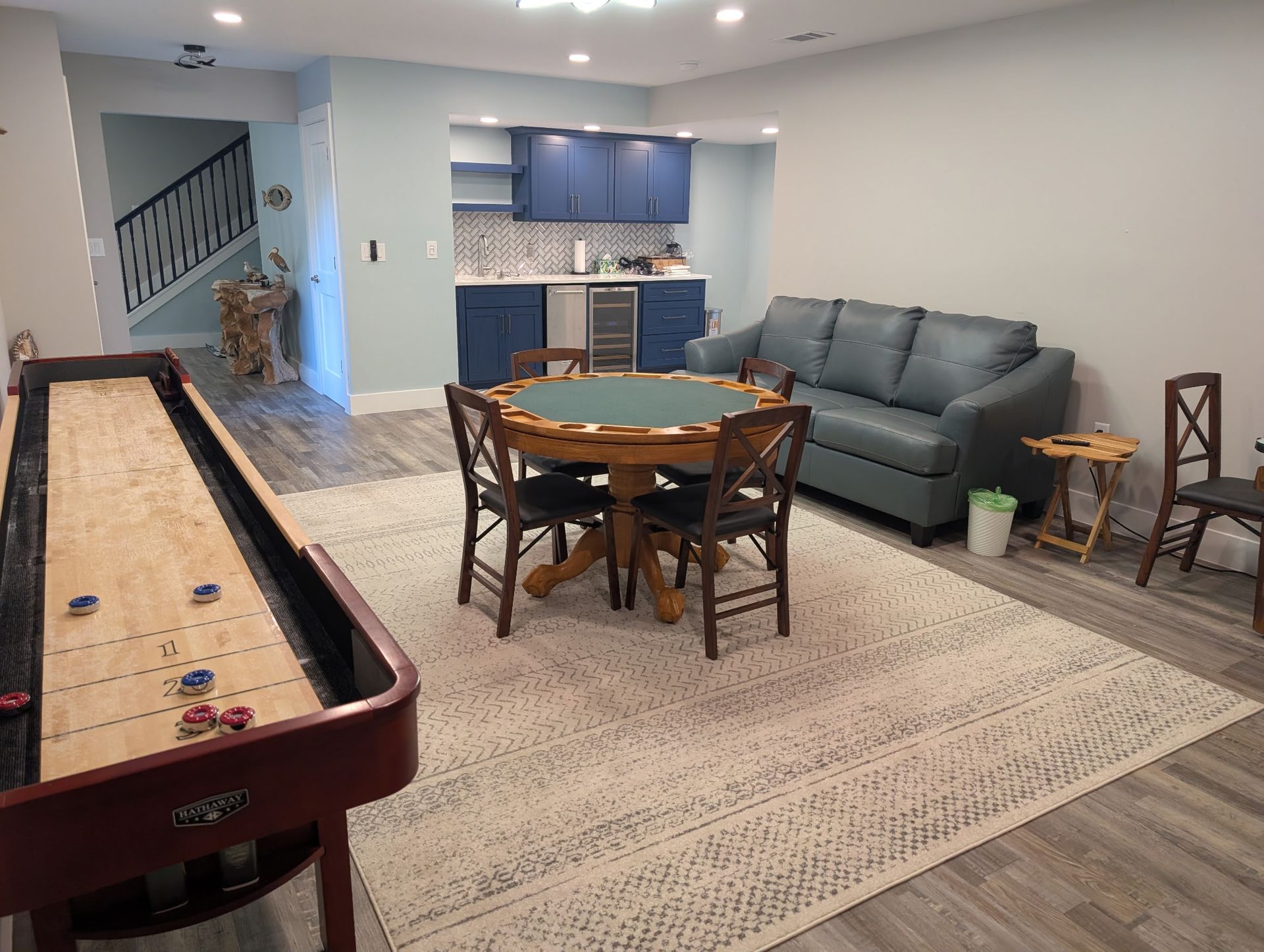 Game room with a shuffleboard table, poker table, blue sofa, and bar area.