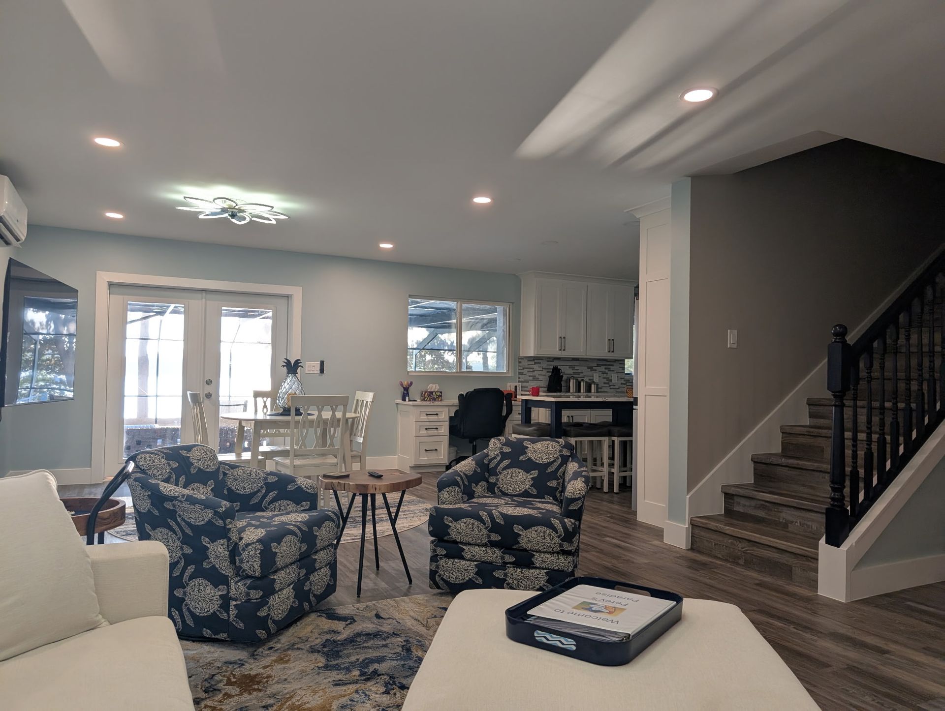 Cozy living room with blue floral armchairs, kitchen, and stairs.