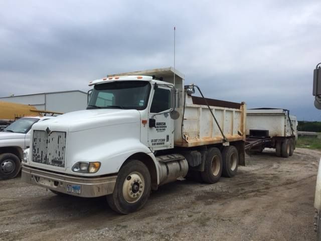 A white dump truck with a trailer attached to it is parked in a dirt lot.
