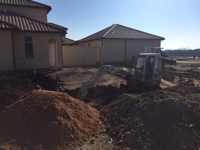 An excavator is digging a hole in the dirt in front of a house