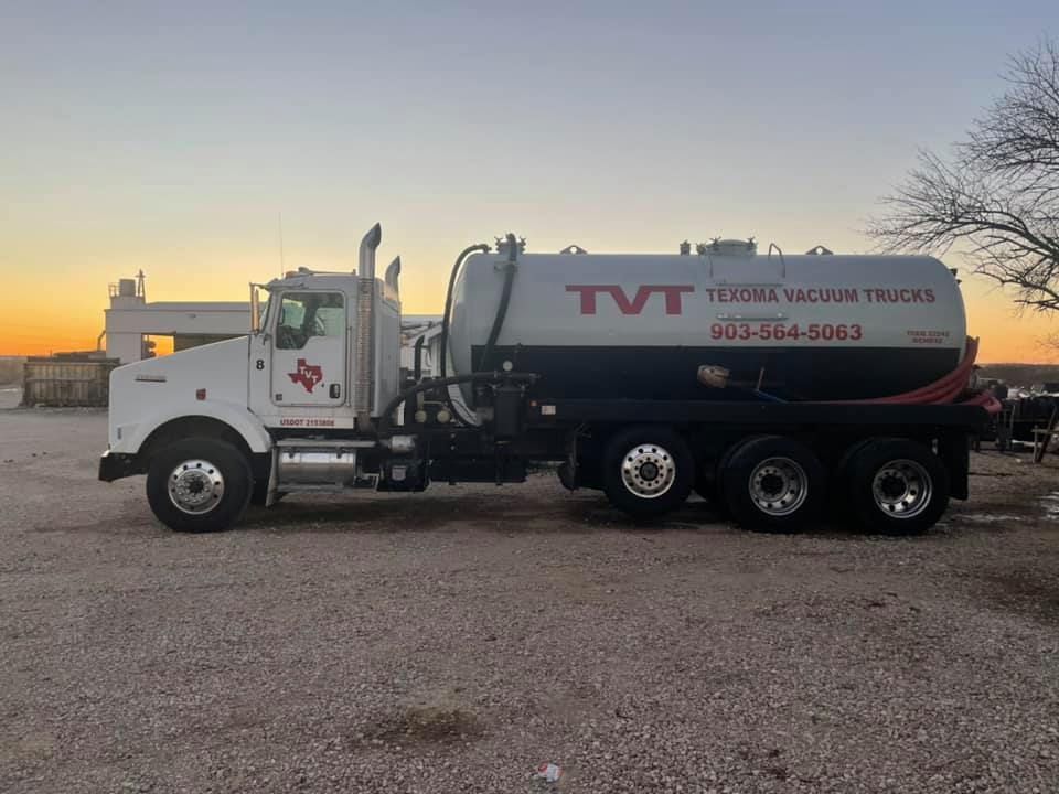 A vacuum truck is parked in a gravel lot at sunset.