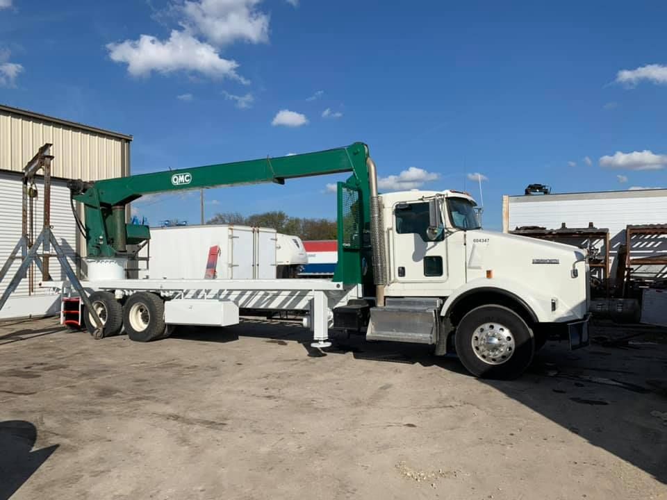 A white truck with a green crane on the back is parked in a parking lot.