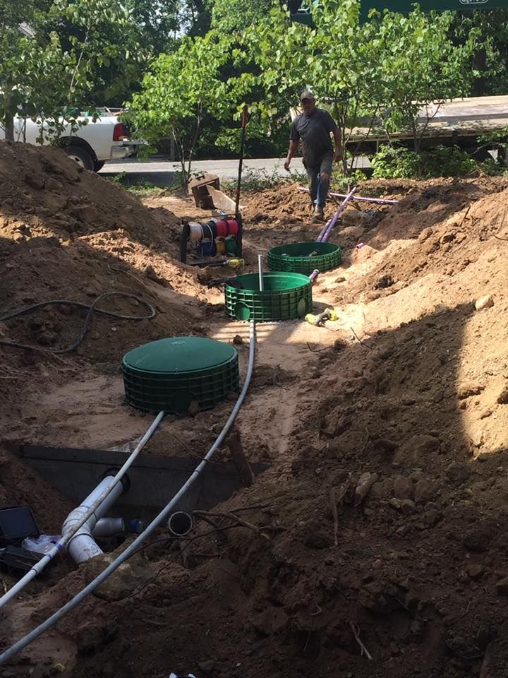 A man is standing in a pile of dirt next to a septic tank.