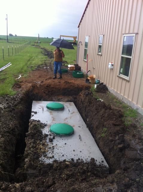 A man is standing in the dirt next to a septic tank.