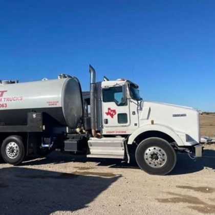 A white truck with a texas logo on the side is parked on a dirt road.