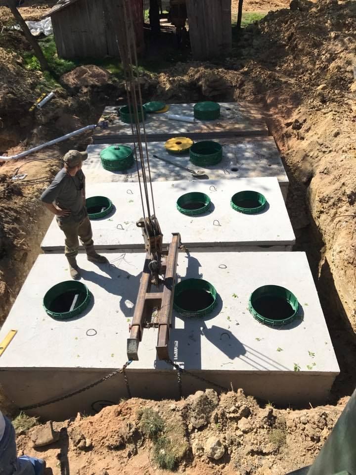 A man is standing next to a concrete septic tank being lifted by a crane.