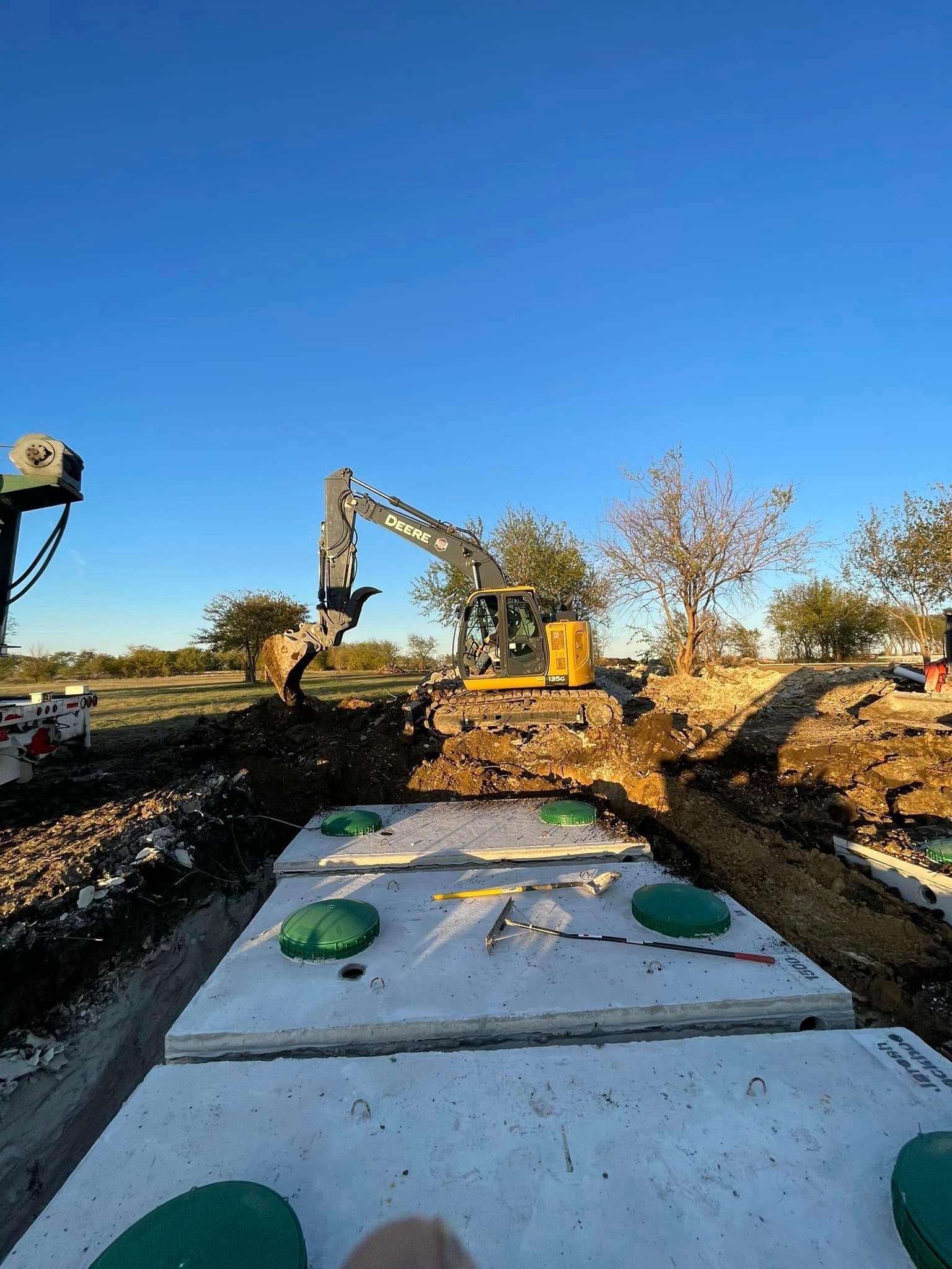 A large excavator is digging a hole in the ground next to a septic tank.