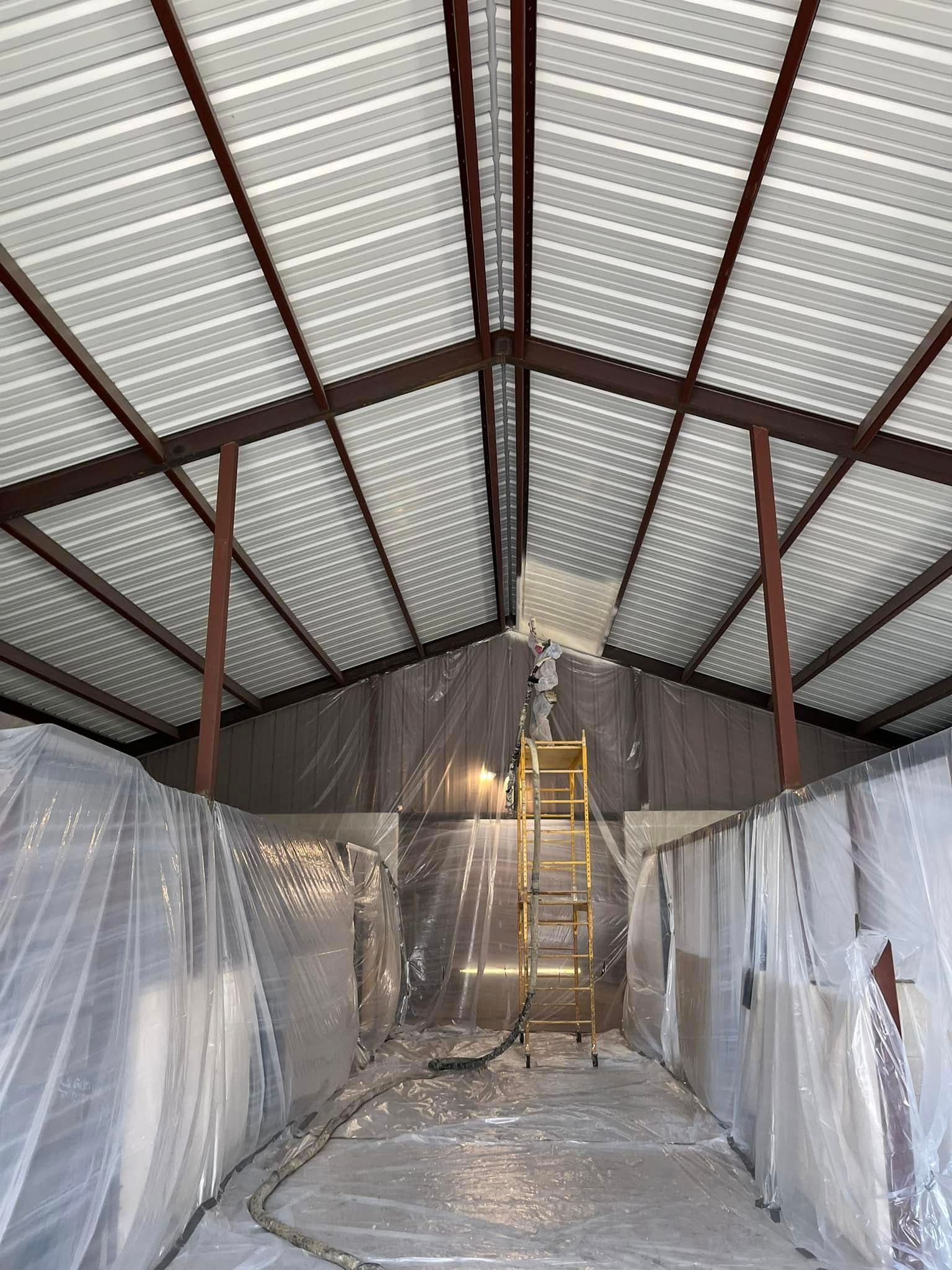 Interior view of a building under construction, plastic sheeting protects walls, metal frame roof. A ladder stands inside.