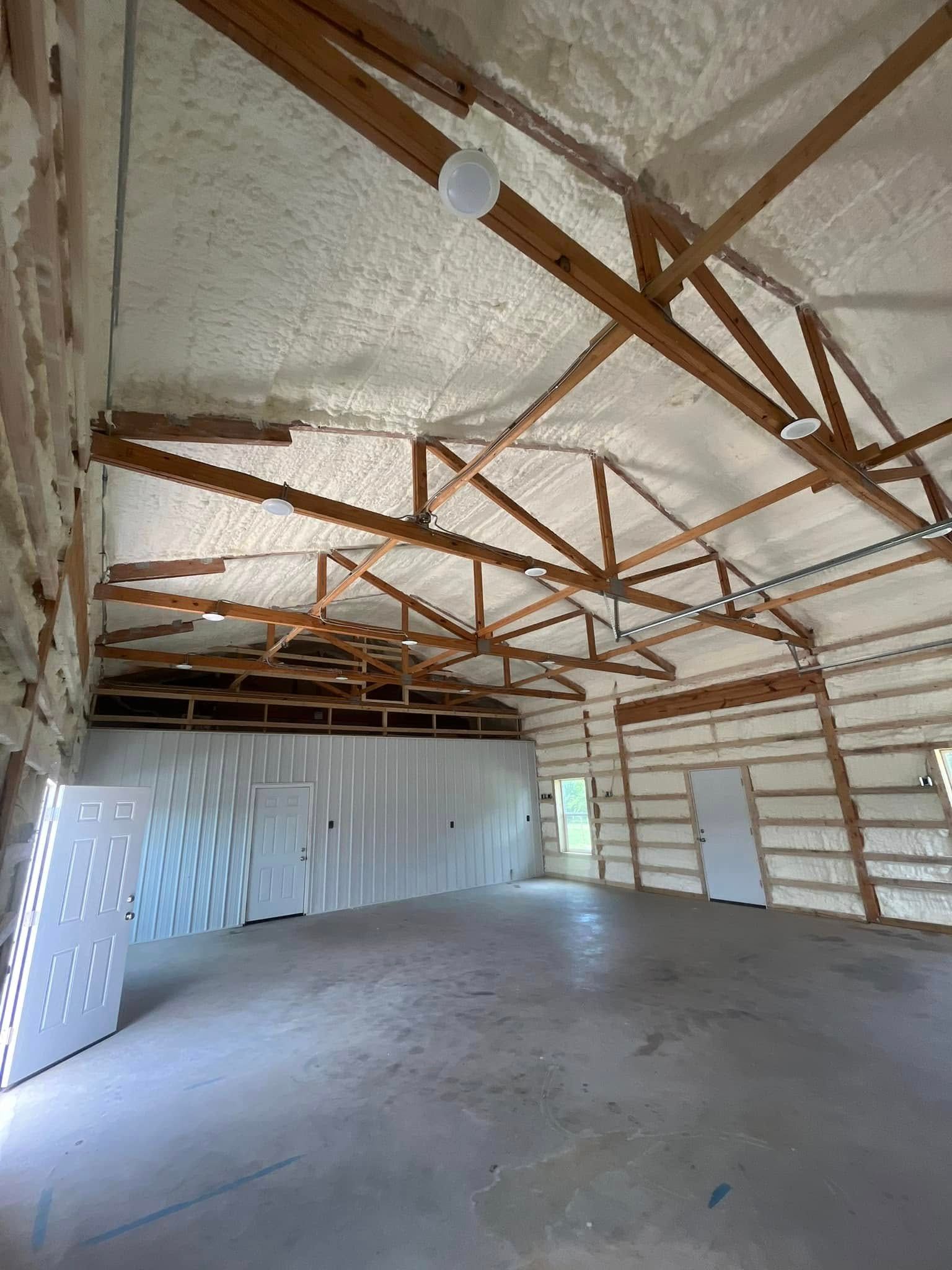 Interior of a large building with spray foam insulation on walls and ceiling, exposed wooden beams, concrete floor.