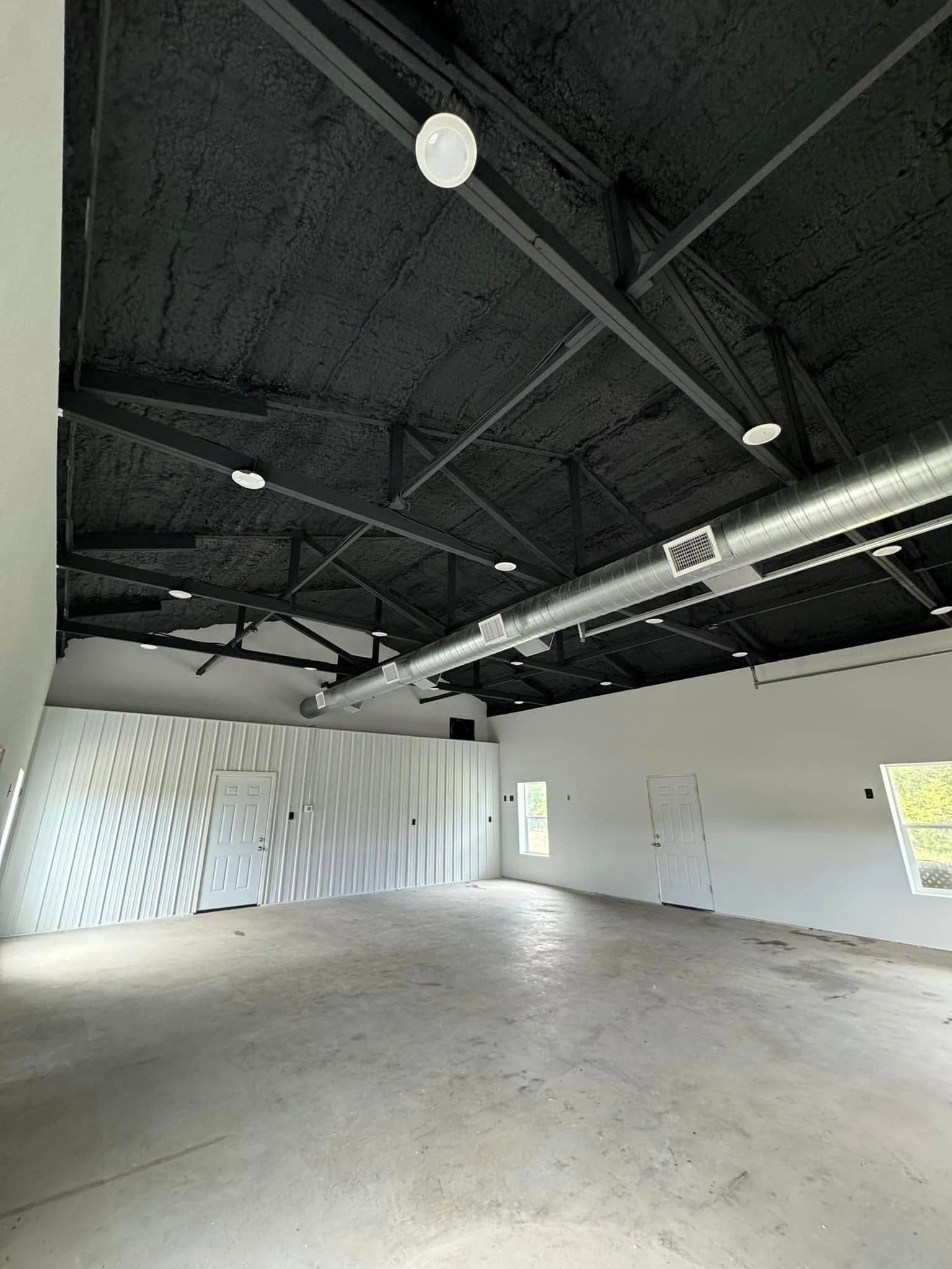 Empty warehouse interior with black ceiling, white walls, and concrete floor.
