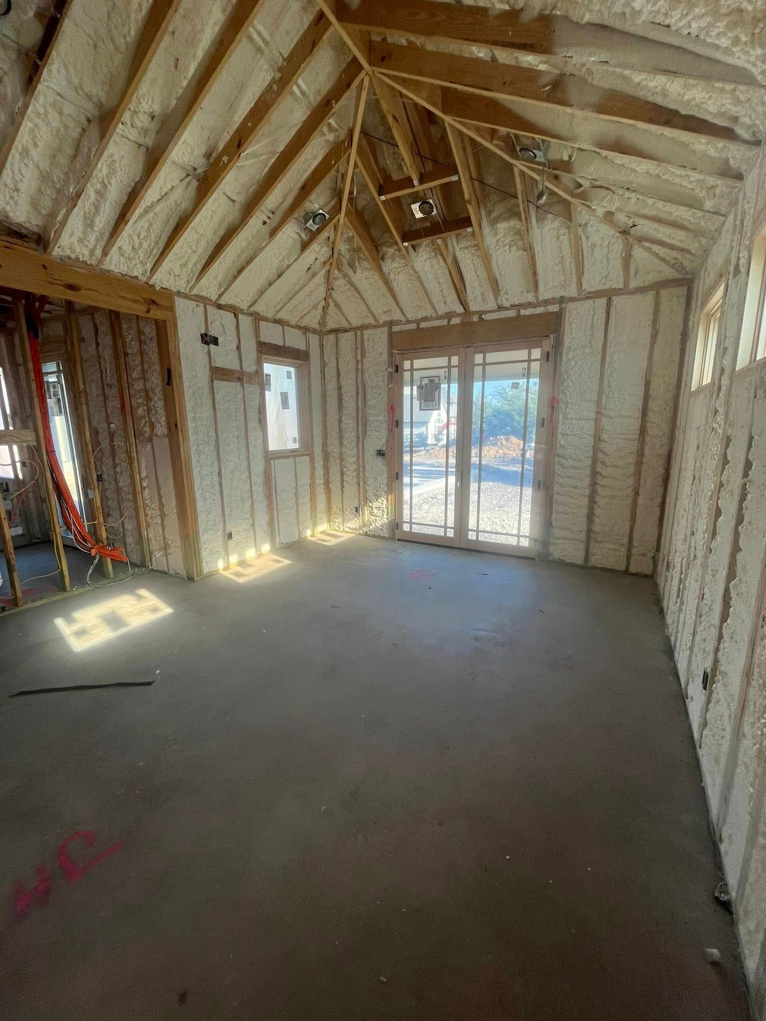 Interior of a building under construction, walls and ceiling insulated with white foam; concrete floor.