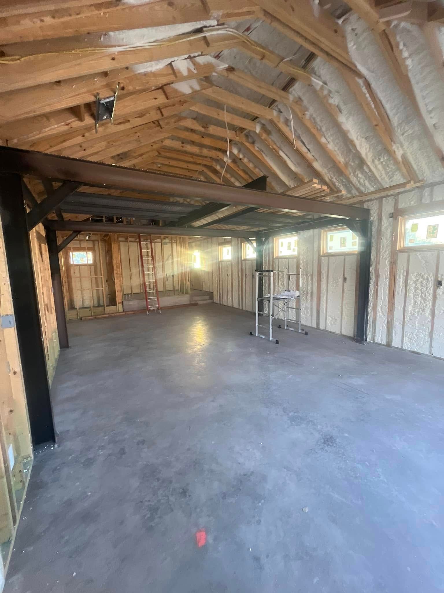 Interior view of a building under construction, featuring wooden framing, concrete floor, and spray foam insulation.