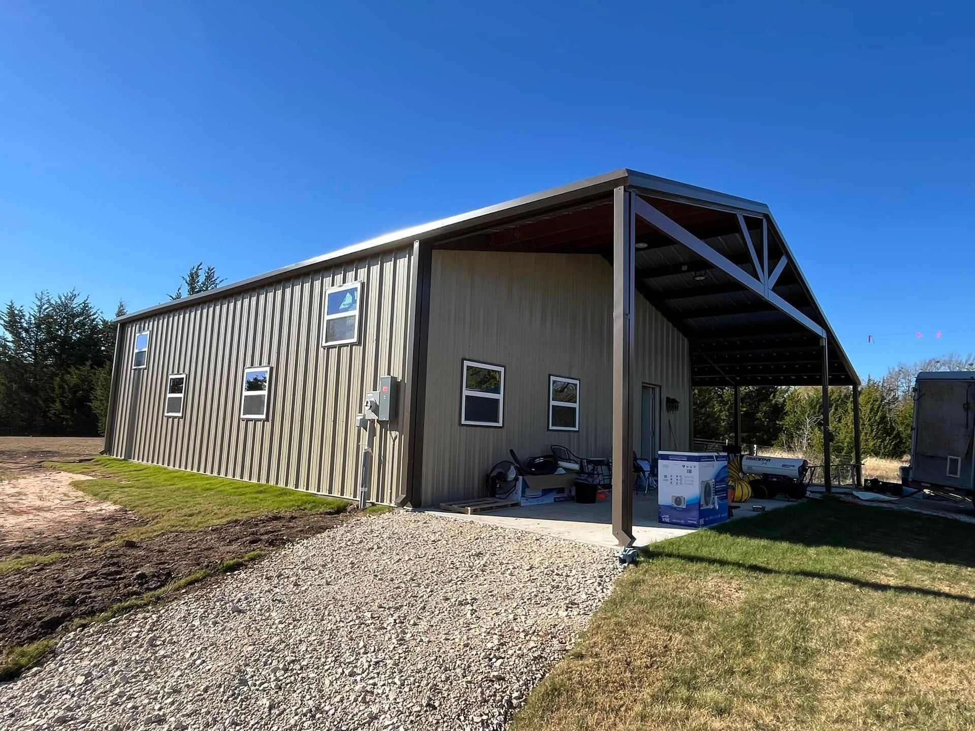 Metal building with brown siding and a gravel driveway under a blue sky.