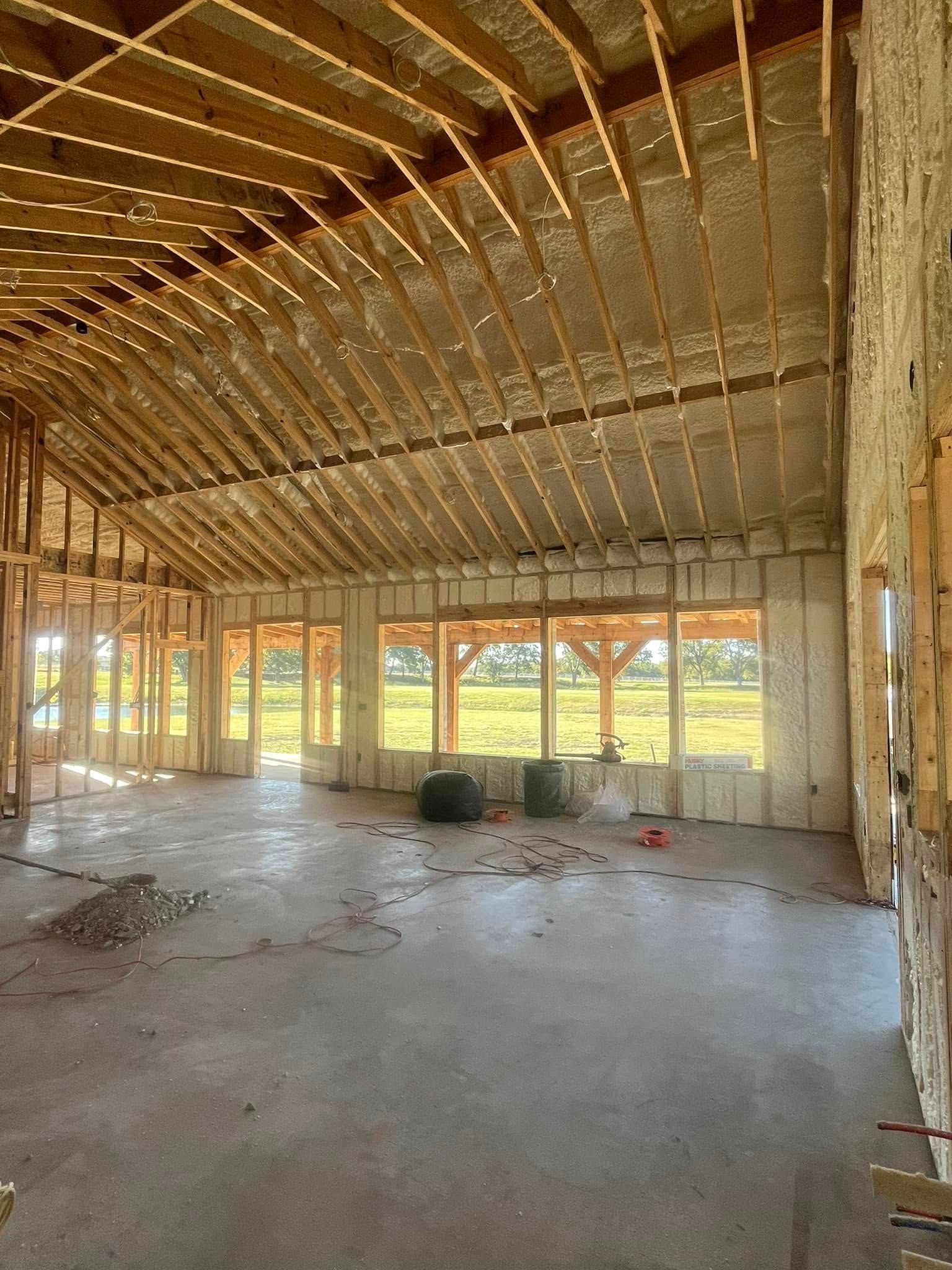 Interior view of a building under construction, with exposed wooden beams, insulation, and a concrete floor.