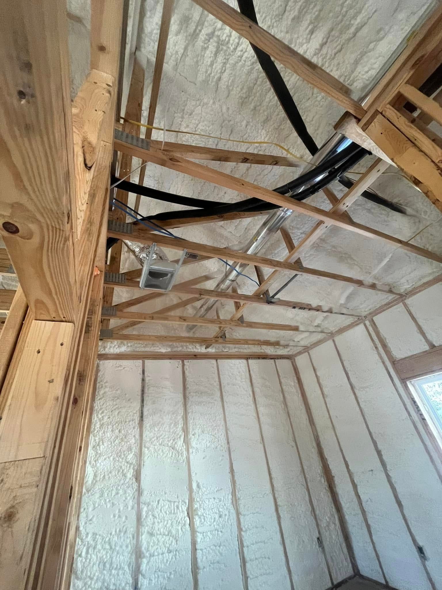 Interior of a building under construction, with wooden beams and spray foam insulation.