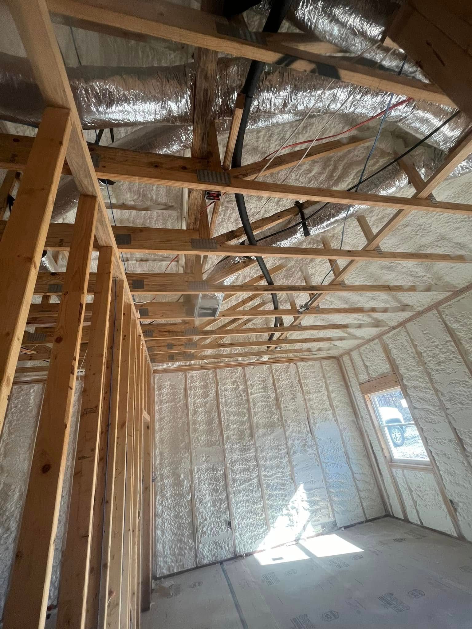 Interior of a building under construction, walls and ceiling insulated with foam, wood framing visible.