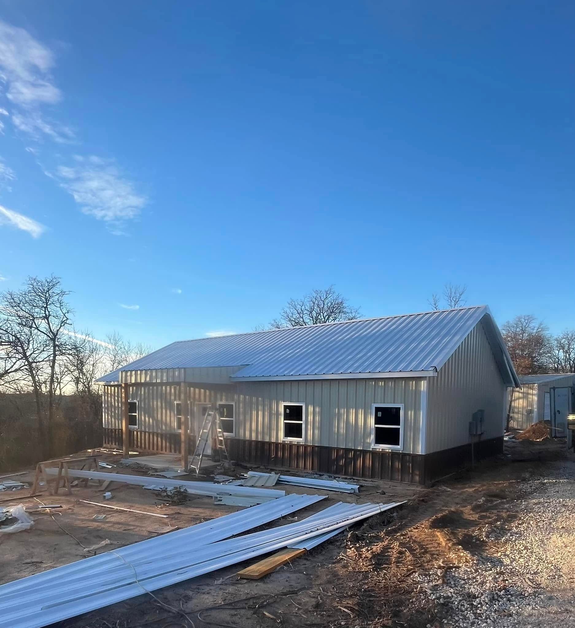 Construction site with a partially built house, metal roof, and blue sky.