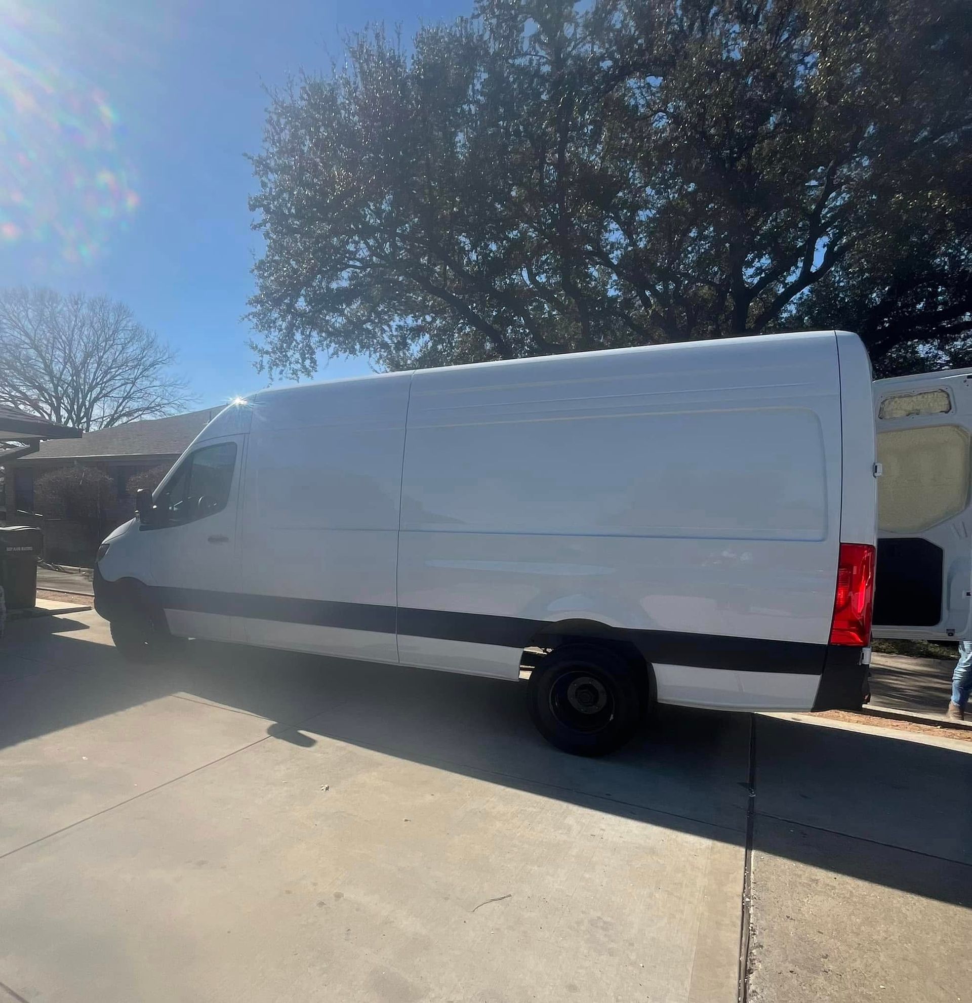 White cargo van parked on a concrete driveway. Sunny day with trees in the background.