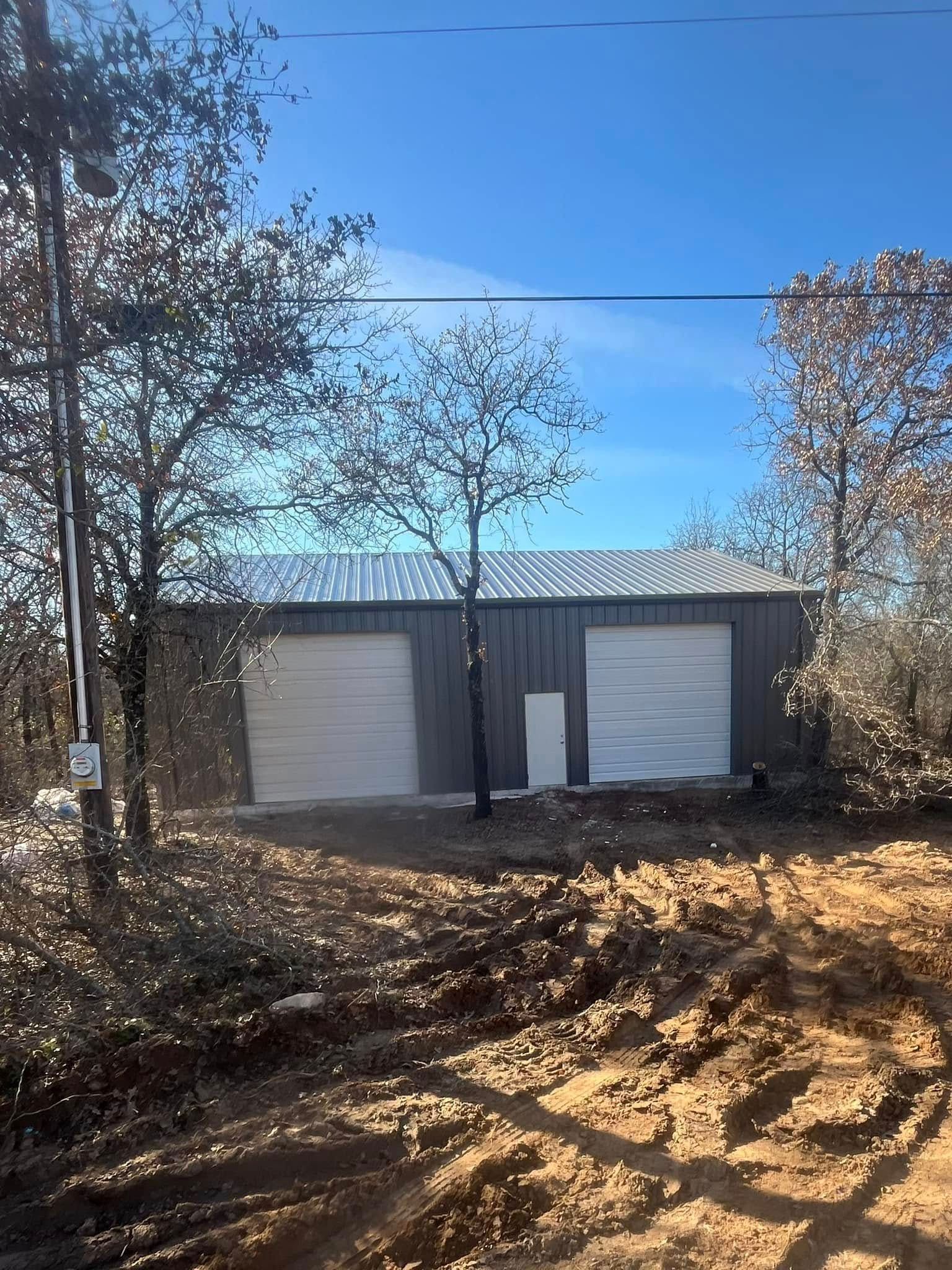 Two-bay metal workshop with silver doors and roof against a clear blue sky.