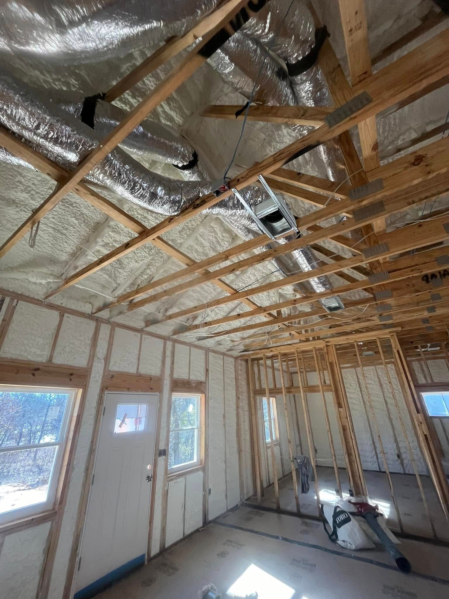 Interior of a room under construction with exposed wooden framework, white insulation, and silver foil.