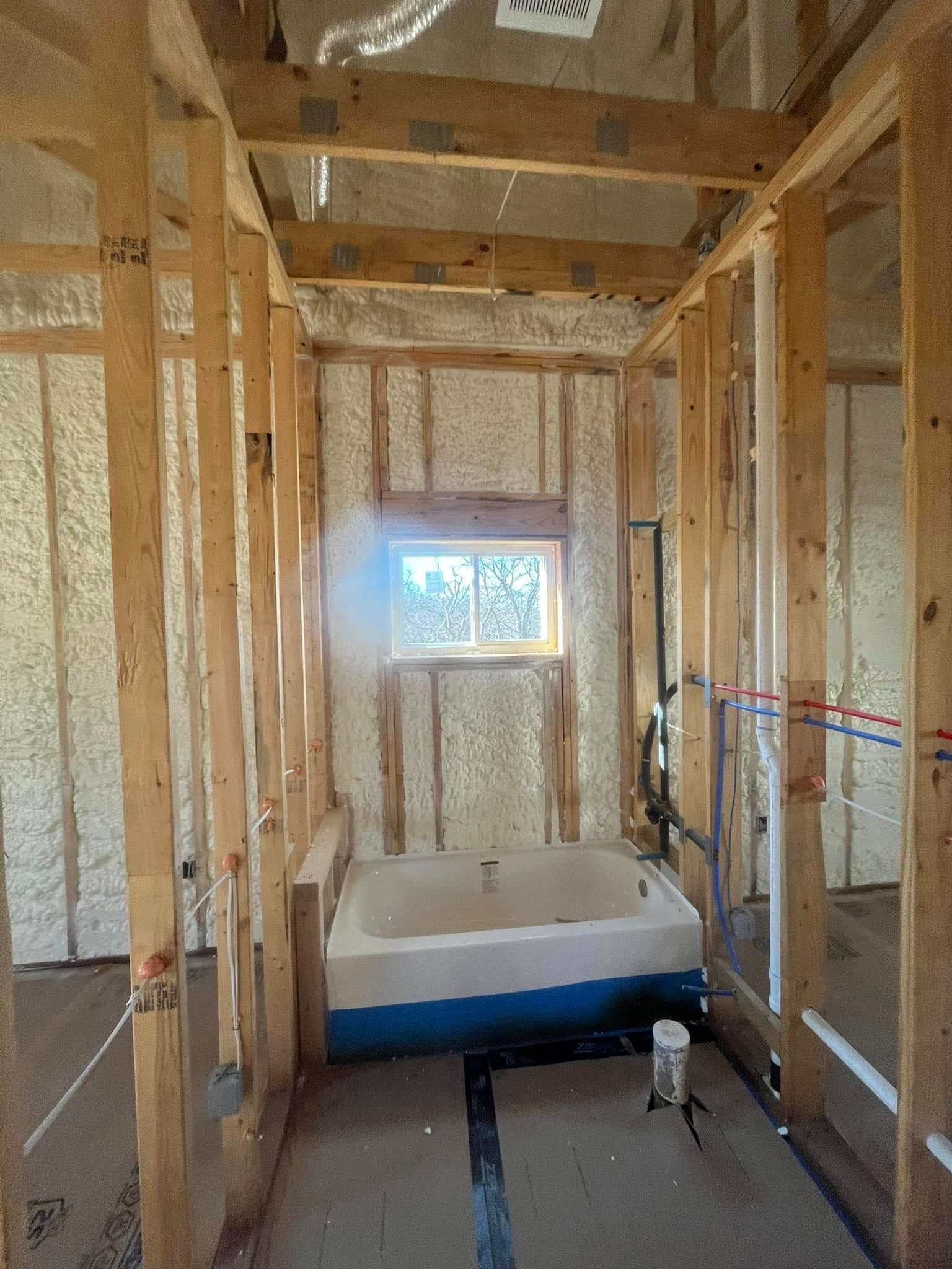 Bathroom framing with a tub, window, and plumbing in progress.